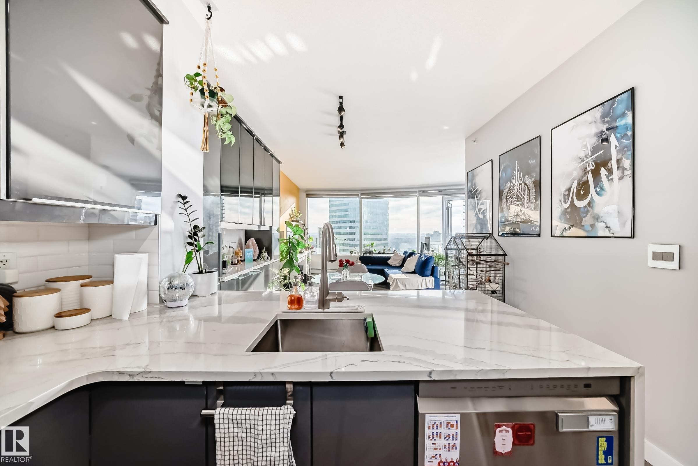 Kitchen with stainless steel dishwasher, light stone countertops, gray cabinets, backsplash, and rail lighting - 2004 10136 104 Street, Edmonton, AB - Indoor Photo Showing Other Room