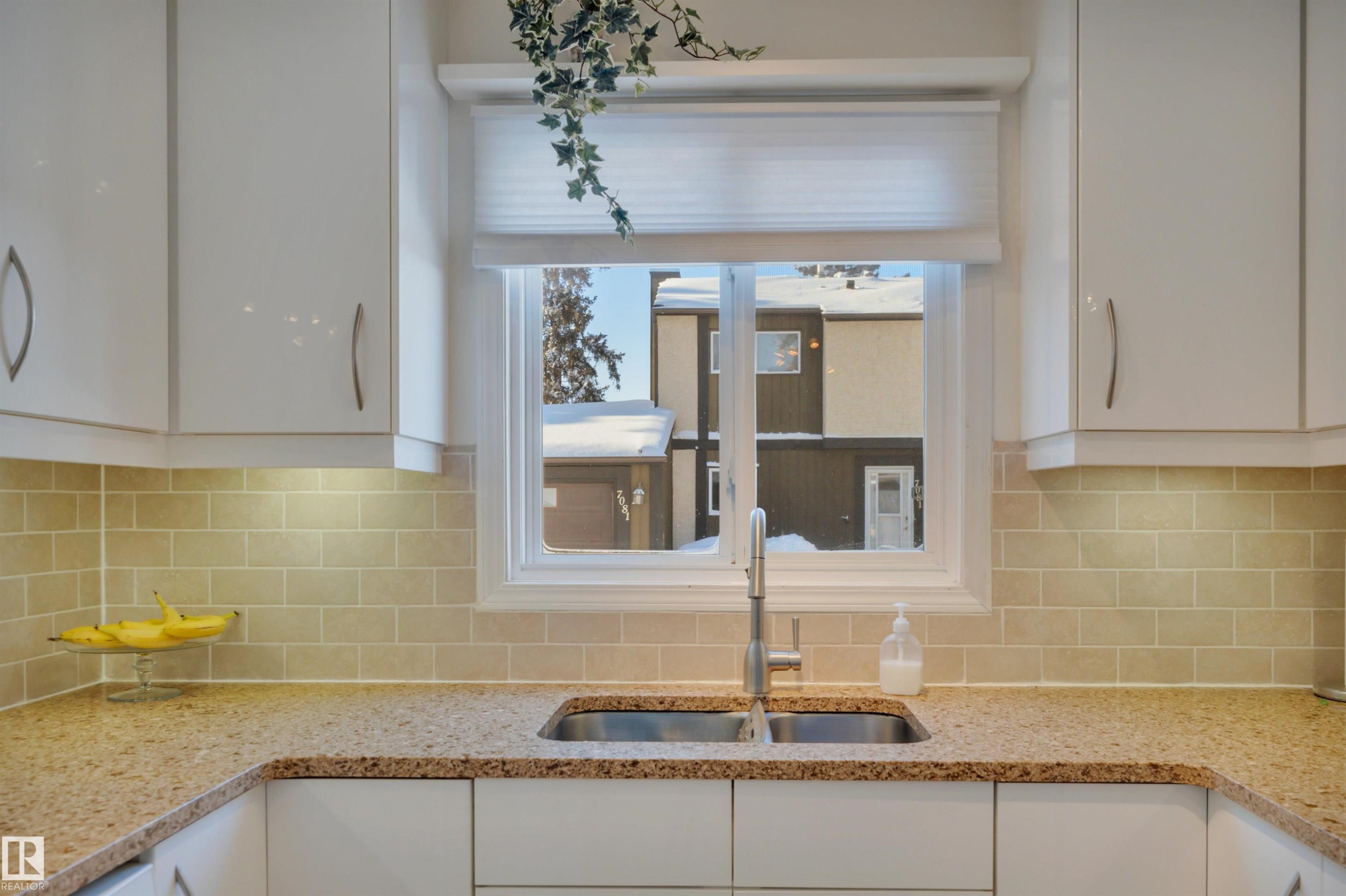 Kitchen view of light stone countertops, white cabinetry, and decorative backsplash - 7075 32 Avenue, Edmonton, AB - Indoor Photo Showing Kitchen With Double Sink