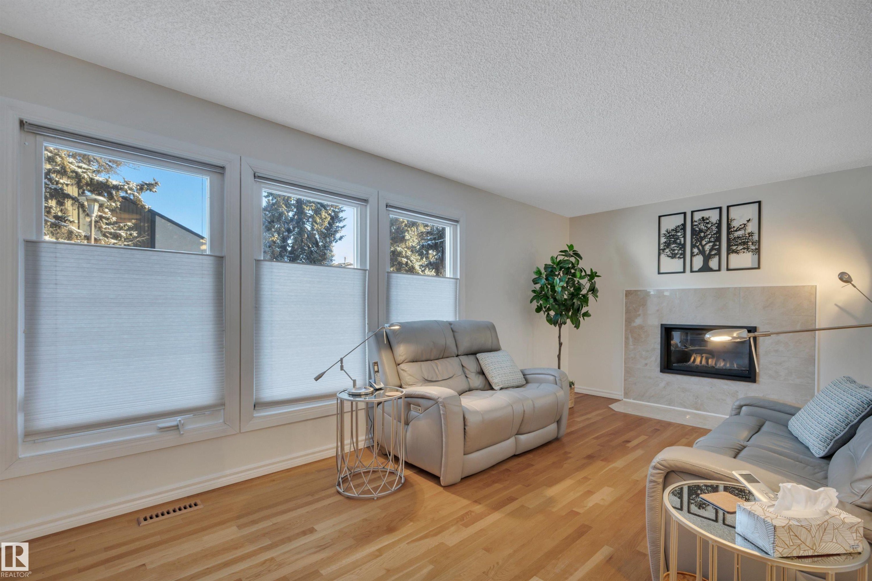 Living area with wood finished floors, a textured ceiling, and a fireplace - 7075 32 Avenue, Edmonton, AB - Indoor Photo Showing Living Room With Fireplace