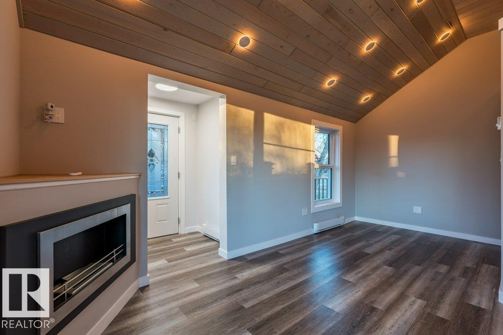 Unfurnished living room featuring a vaulted wood ceiling, dark wood-style flooring, a baseboard radiator, a fireplace, and recessed lighting - 4713 48 Avenue, Wetaskiwin, AB - Indoor With Fireplace