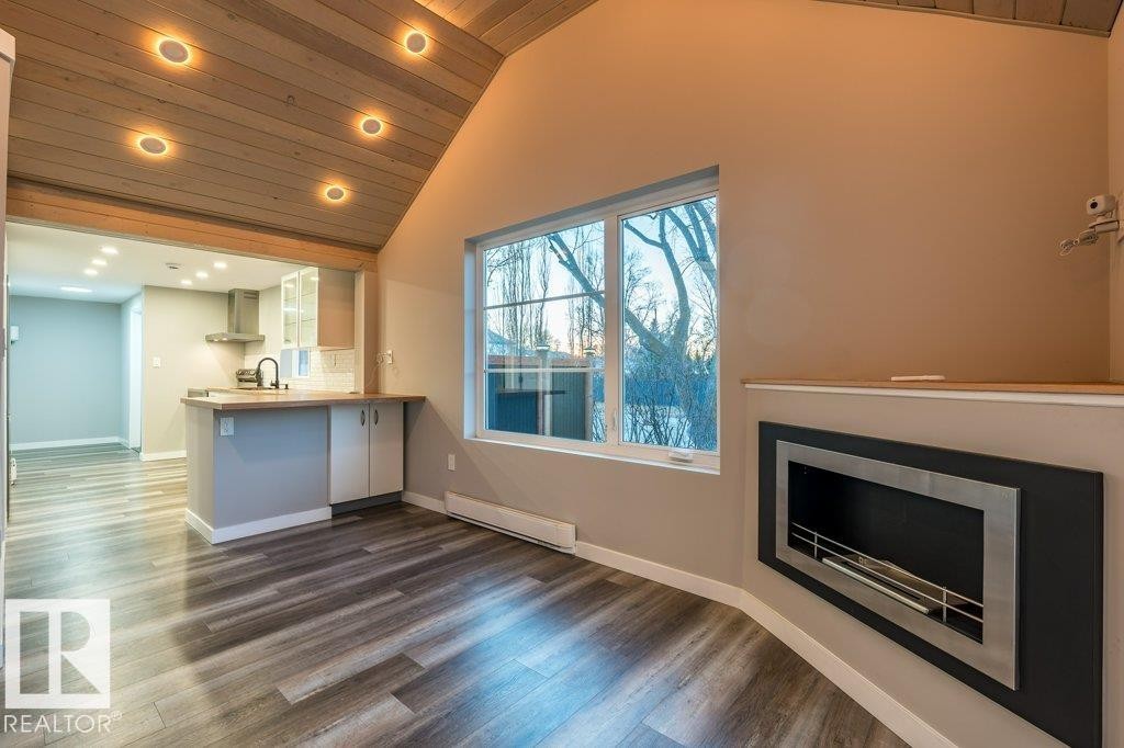 Unfurnished living room featuring a vaulted wooden ceiling, a baseboard heating unit, a glass covered fireplace, dark wood-type flooring, and recessed lighting - 4713 48 Avenue, Wetaskiwin, AB - Indoor With Fireplace