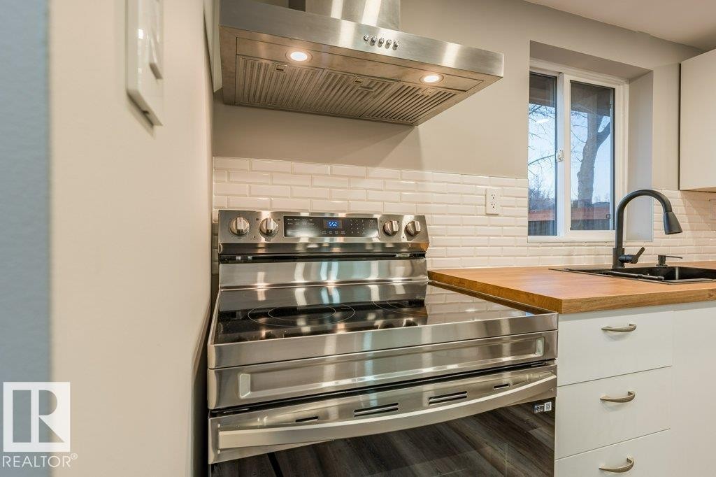 Kitchen with electric stove, extractor fan, white cabinets, wooden counters, and decorative backsplash - 4713 48 Avenue, Wetaskiwin, AB - Indoor Photo Showing Kitchen