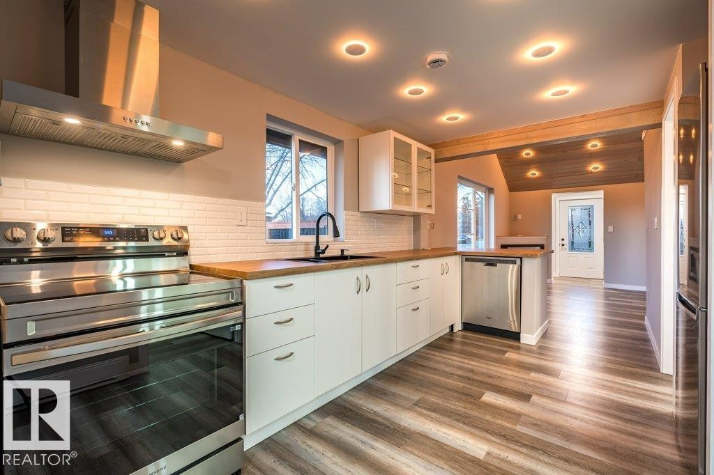 Kitchen with stainless steel appliances, glass fronted cabinets, white cabinets, a peninsula, and dark wood-style flooring - 4713 48 Avenue, Wetaskiwin, AB - Indoor Photo Showing Kitchen With Upgraded Kitchen
