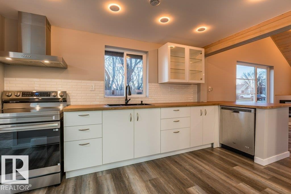 Kitchen with white cabinetry, stainless steel appliances, glass insert cabinets, a peninsula, and healthy amount of natural light - 4713 48 Avenue, Wetaskiwin, AB - Indoor Photo Showing Kitchen
