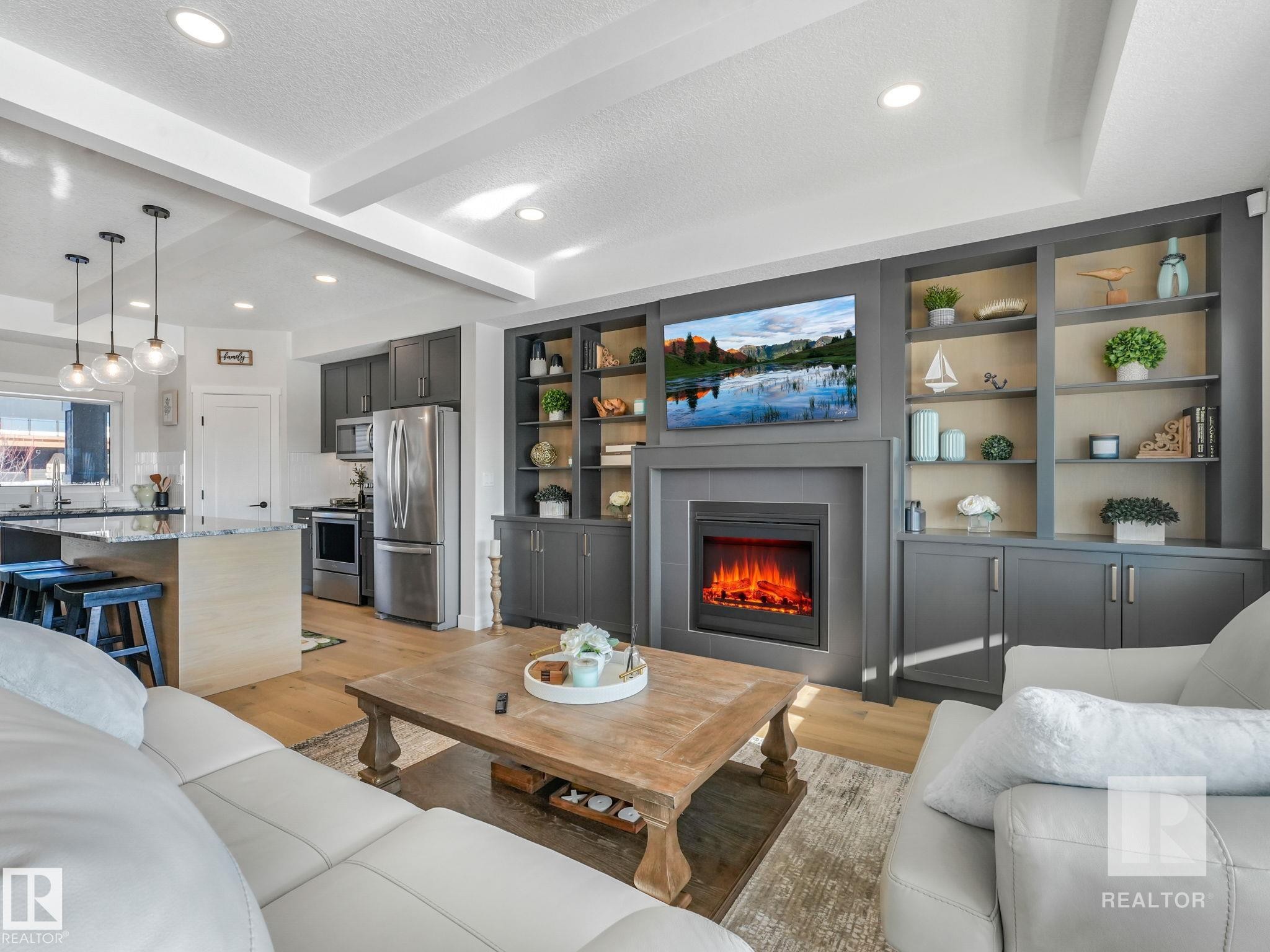 Living area with light wood-type flooring, beam ceiling, a textured ceiling, a tile fireplace, and built in features - 209 55101 Ste. Anne Trail, Rural Lac Ste. Anne County, AB - Indoor Photo Showing Living Room With Fireplace