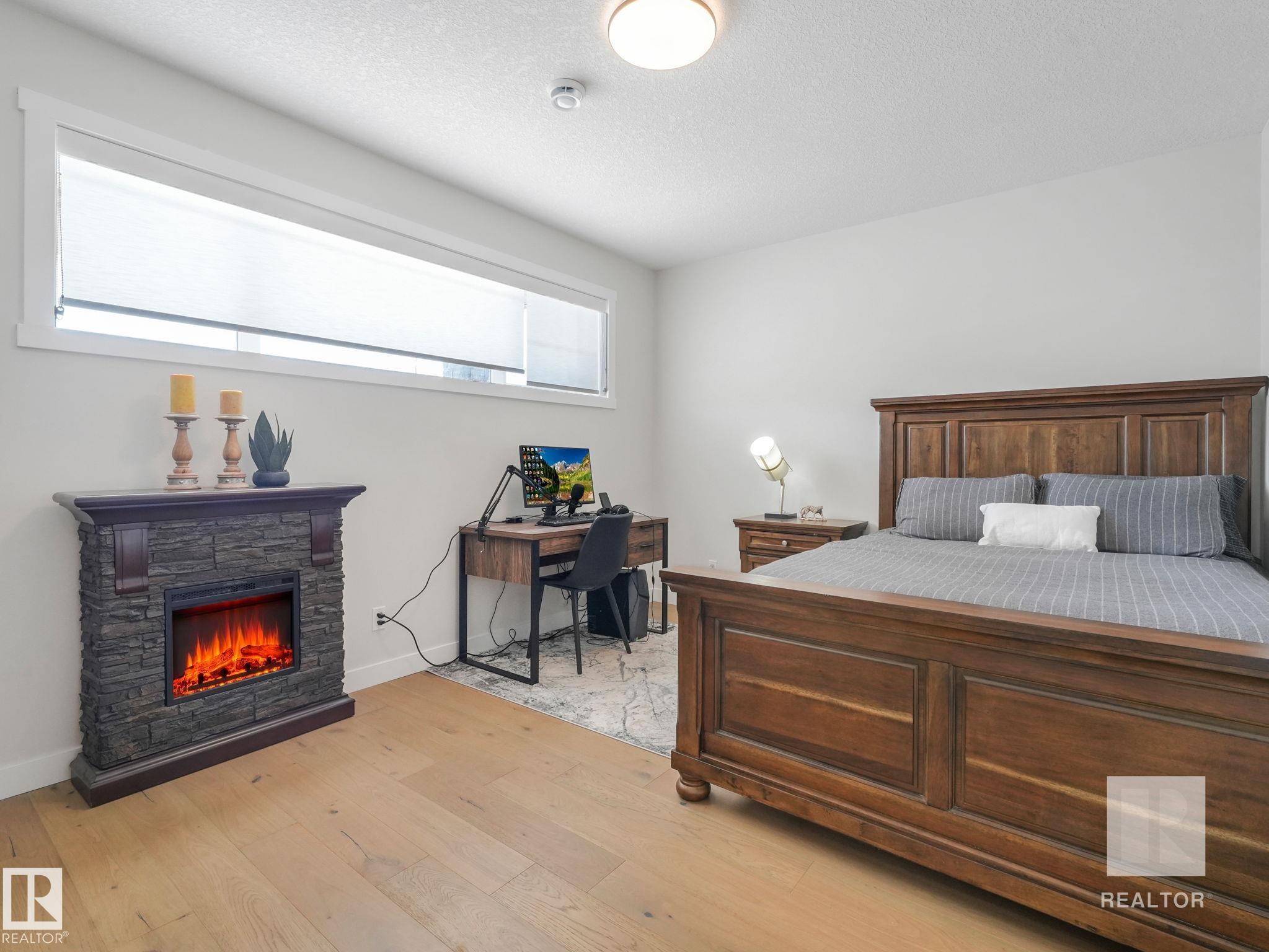 Bedroom featuring light wood-style flooring, a fireplace, a textured ceiling, and an office area - 209 55101 Ste. Anne Trail, Rural Lac Ste. Anne County, AB - Indoor Photo Showing Bedroom With Fireplace