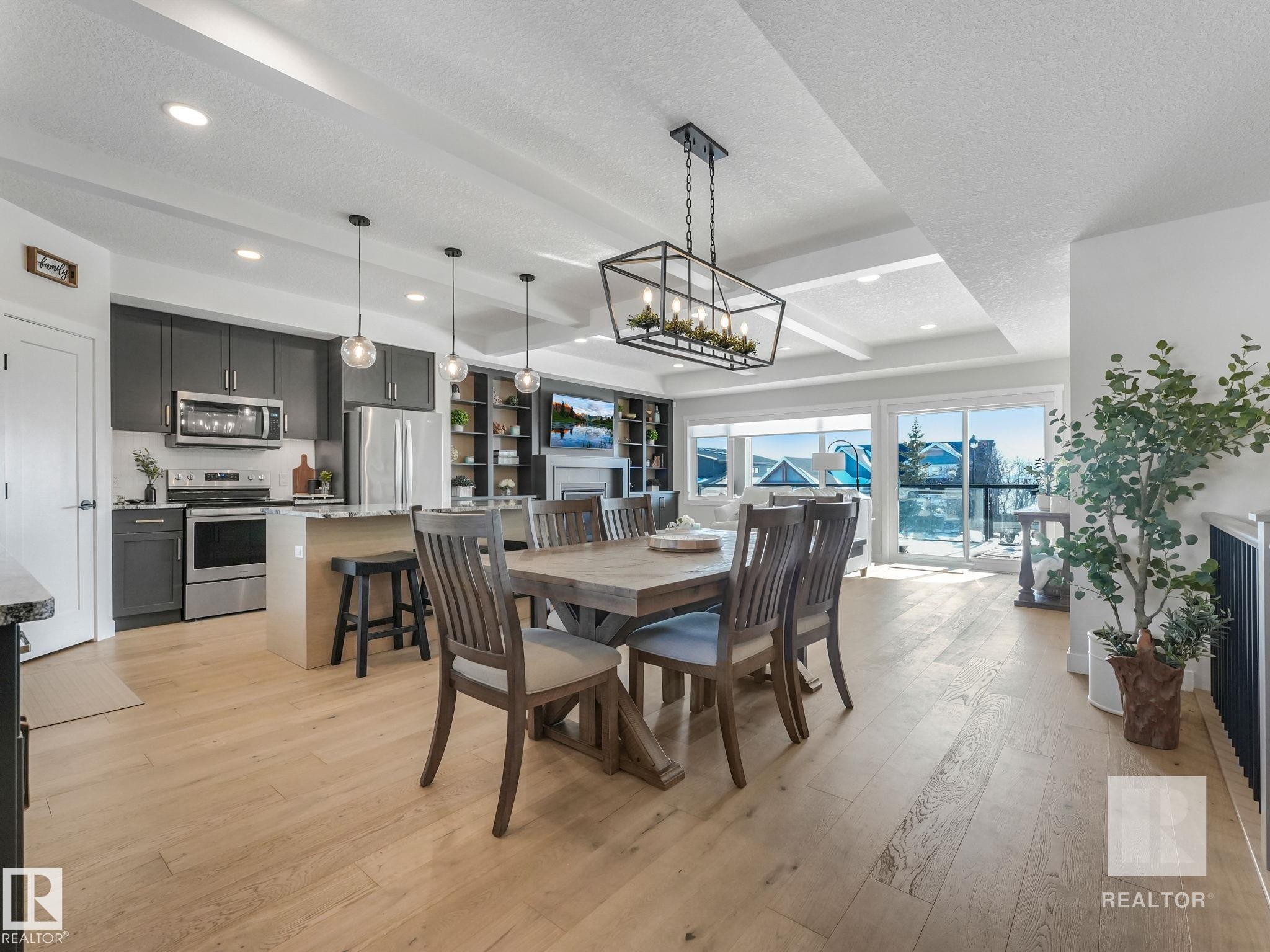 Dining space with a textured ceiling, light wood-style floors, suspended lighting, a fireplace, and beamed ceiling - 209 55101 Ste. Anne Trail, Rural Lac Ste. Anne County, AB - Indoor