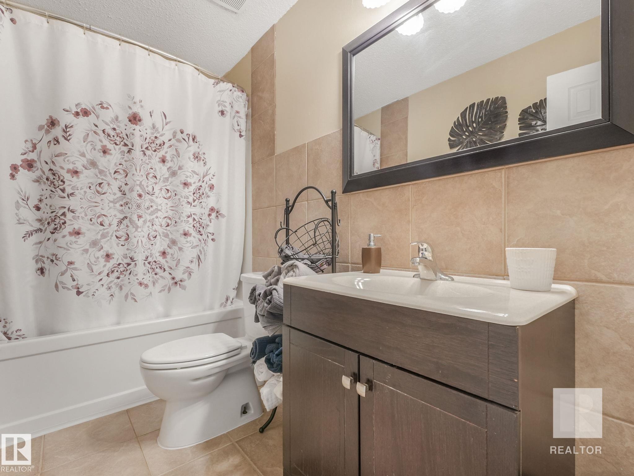 Bathroom featuring vanity, shower / bath combo with shower curtain, tile walls, light tile patterned floors, and a textured ceiling - 4504 48 Avenue, Onoway, AB - Indoor Photo Showing Bathroom