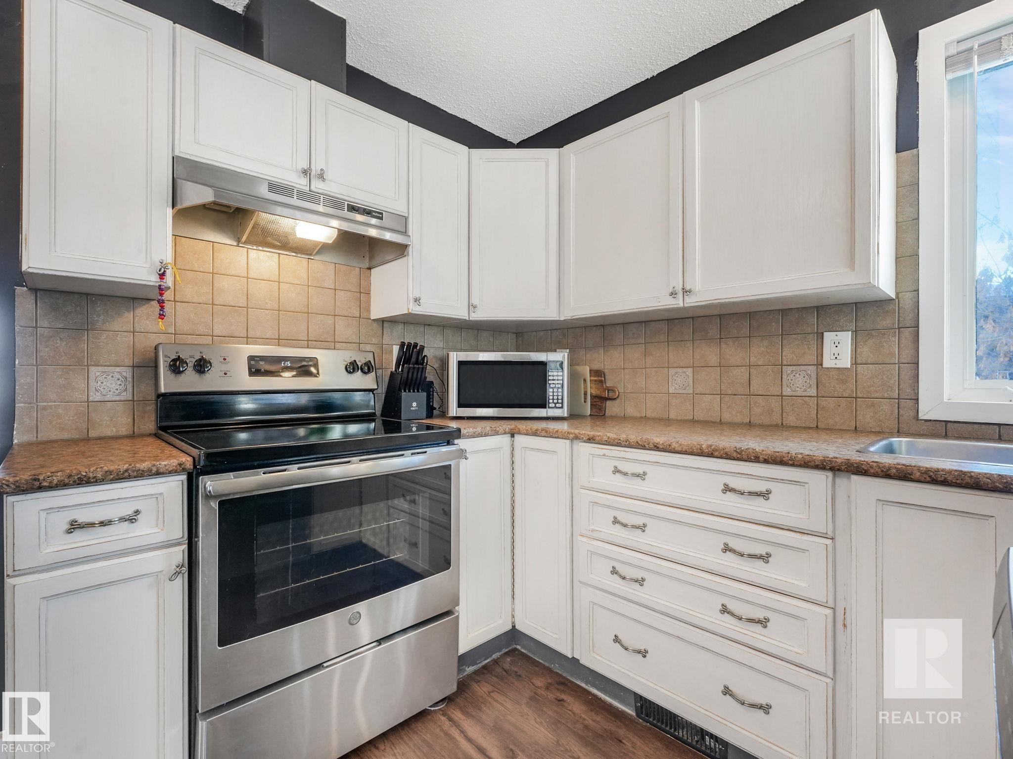 Kitchen featuring stainless steel appliances, white cabinets, dark wood-style floors, and a textured ceiling - 4504 48 Avenue, Onoway, AB - Indoor Photo Showing Kitchen