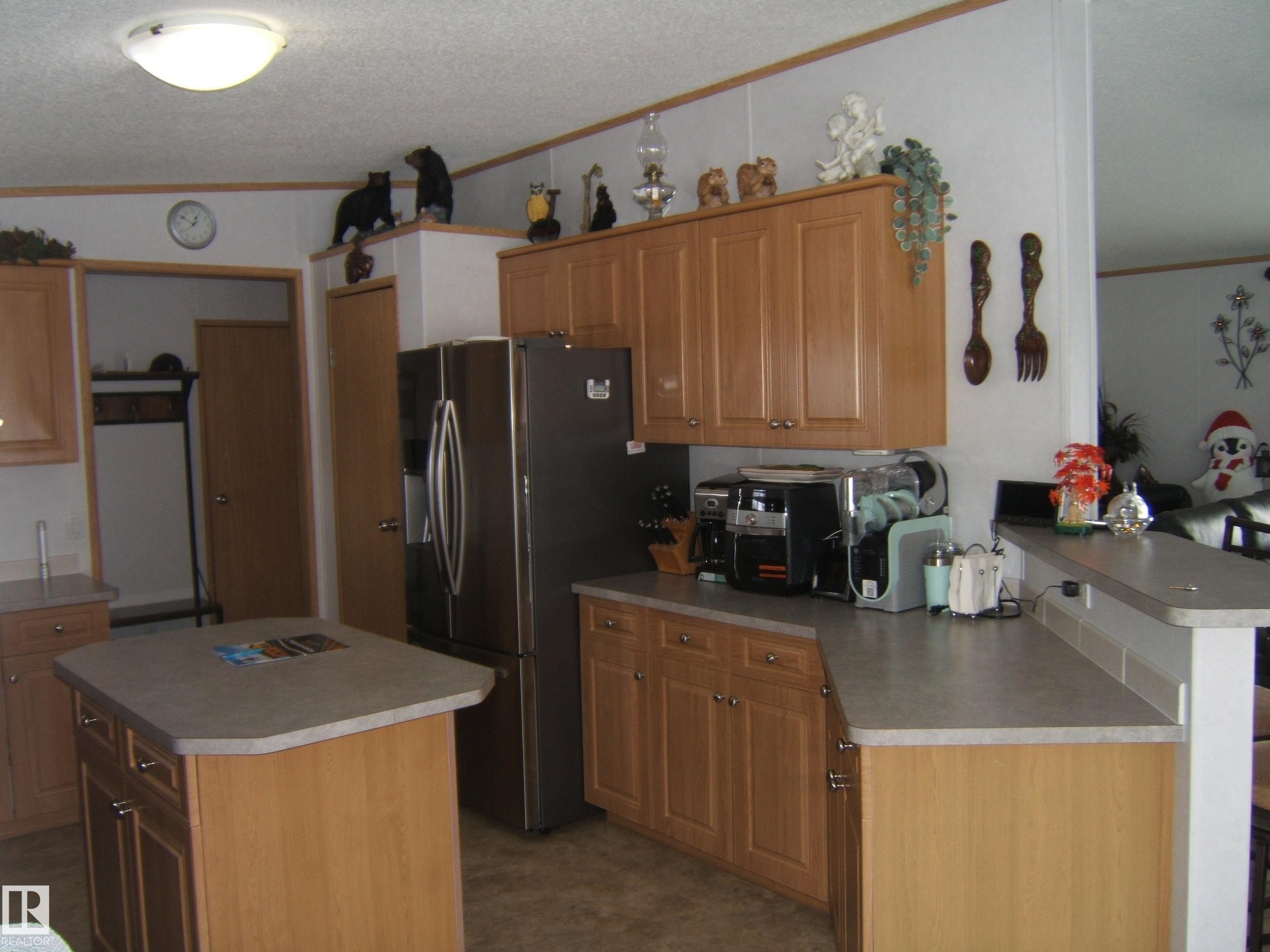 Kitchen with crown molding, wood finish cabinetry, a peninsula, stainless steel fridge with ice dispenser, and a kitchen island - 125076 Twp Rd 540, Rural Two Hills County, AB - Indoor Photo Showing Kitchen