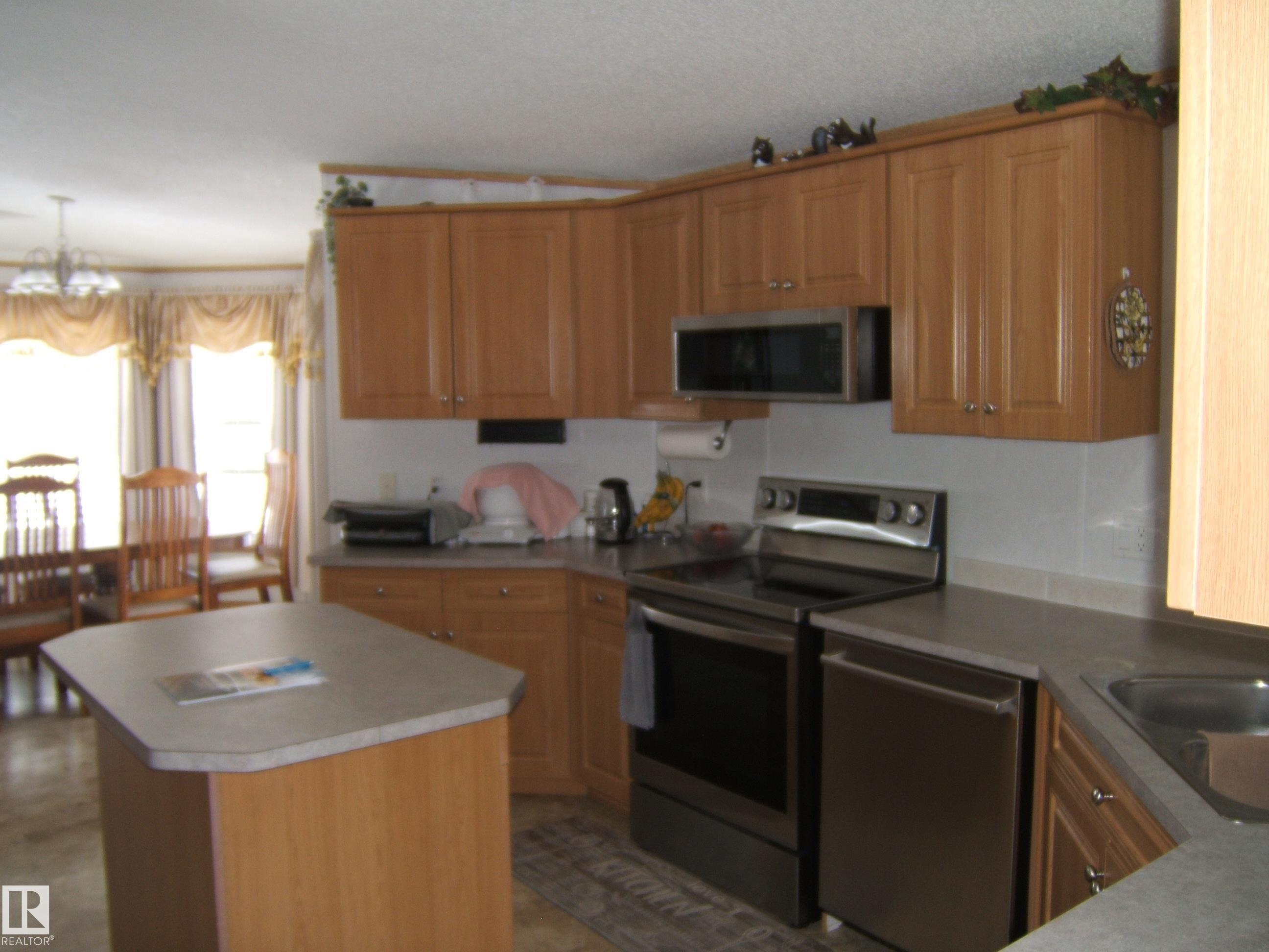 Kitchen with stainless steel appliances, a center island, suspended lighting, wood finish cabinetry, and light countertops - 125076 Twp Rd 540, Rural Two Hills County, AB - Indoor Photo Showing Kitchen