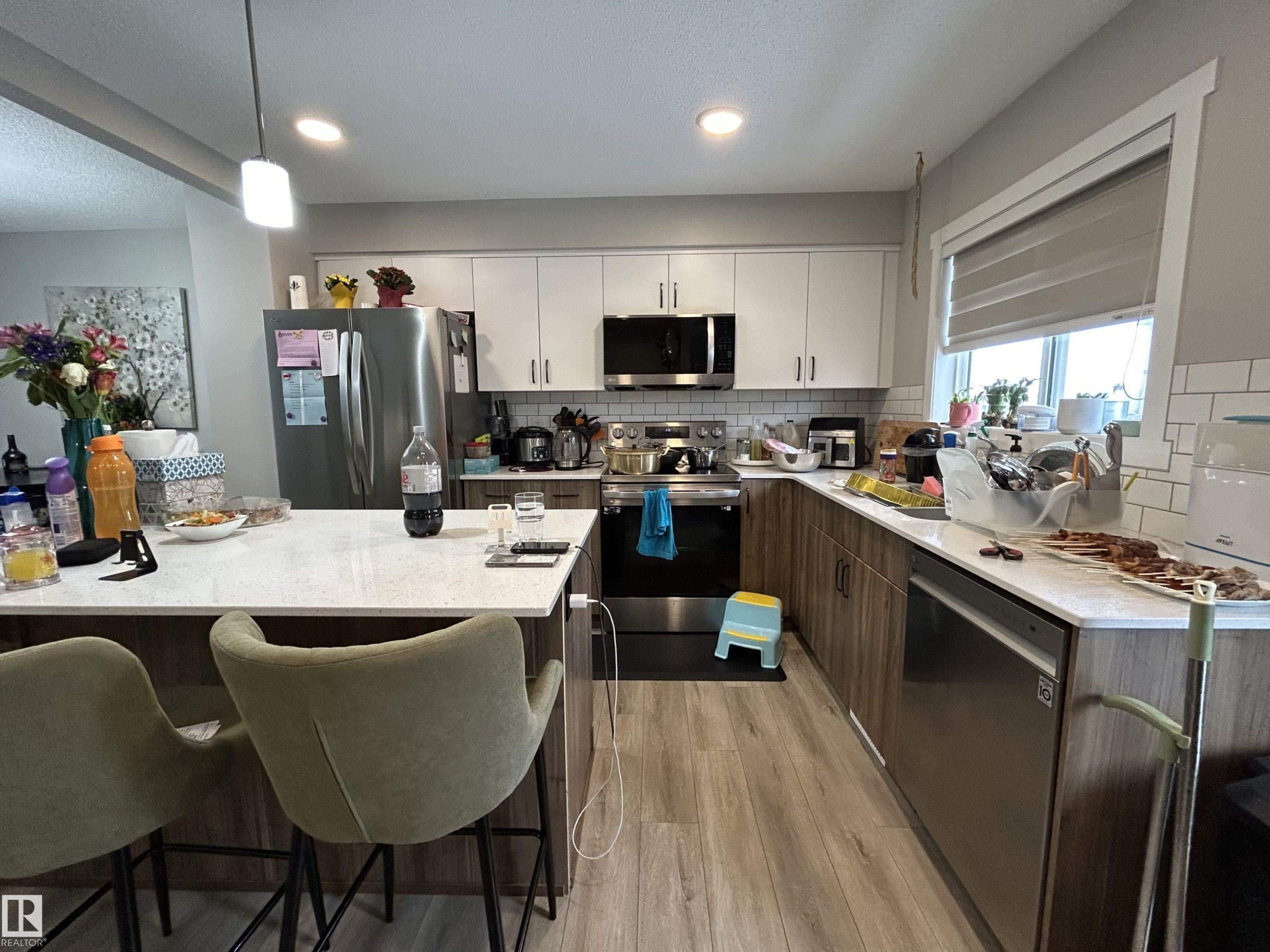 Kitchen featuring stainless steel appliances, a kitchen bar, backsplash, light wood finished floors, and light stone counters - 120 1530 Tamarack Boulevard, Edmonton, AB - Indoor Photo Showing Kitchen With Stainless Steel Kitchen With Double Sink With Upgraded Kitchen