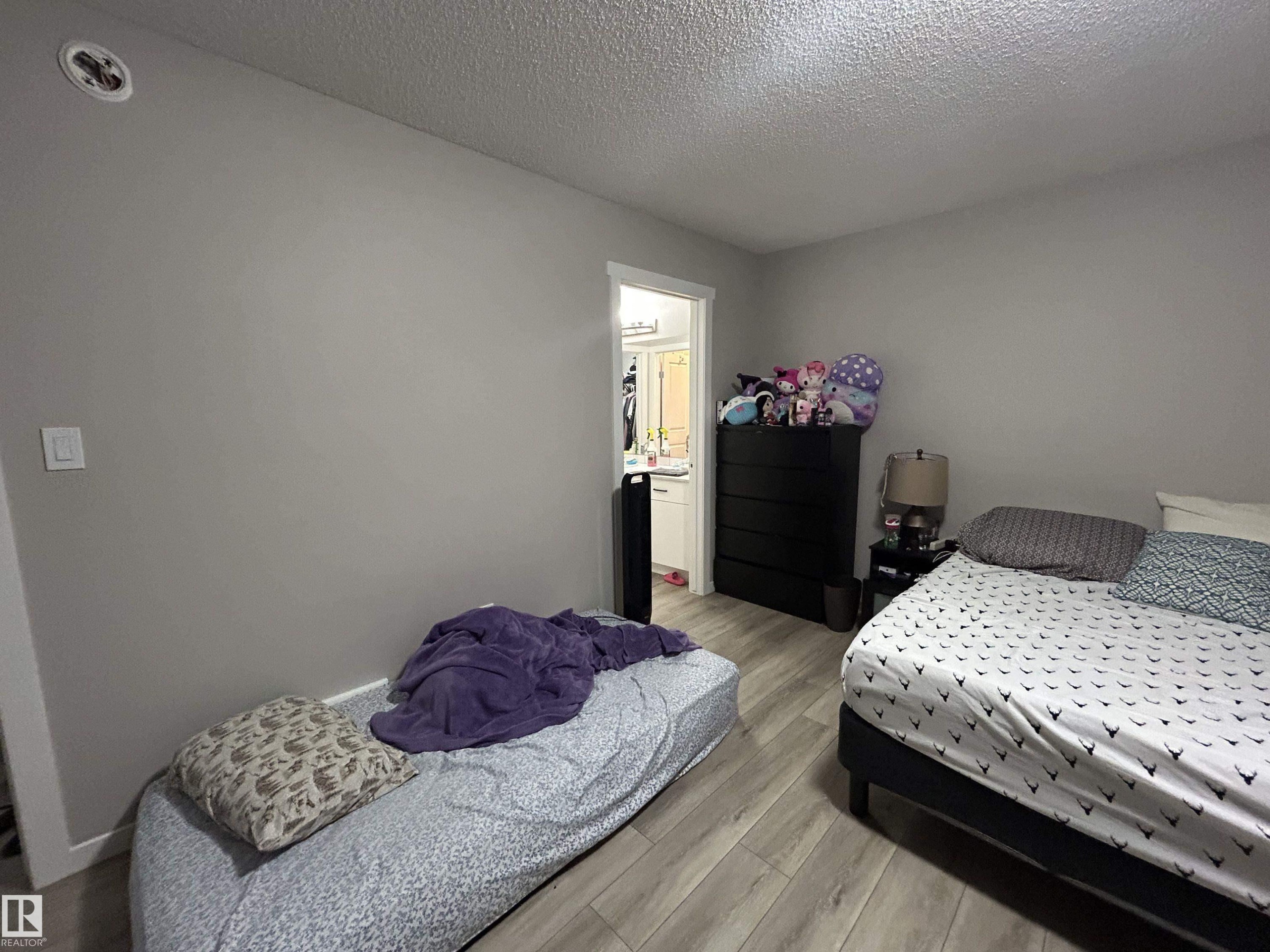 Bedroom featuring light wood finished floors, a textured ceiling, and ensuite bathroom - 120 1530 Tamarack Boulevard, Edmonton, AB - Indoor Photo Showing Bedroom
