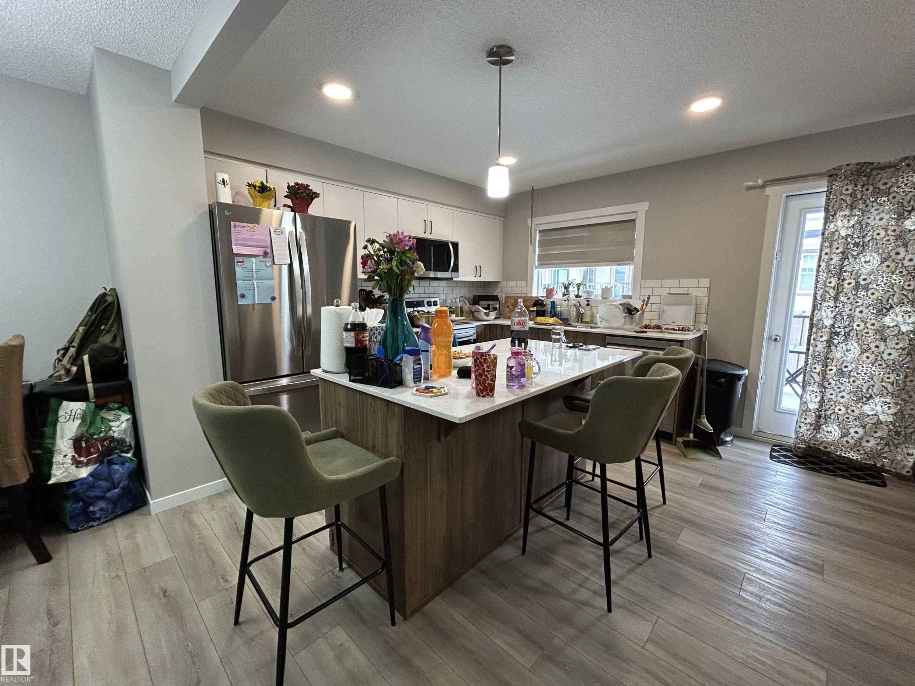 Kitchen featuring a kitchen bar, a kitchen island, stainless steel appliances, tasteful backsplash, and a textured ceiling - 120 1530 Tamarack Boulevard, Edmonton, AB - Indoor
