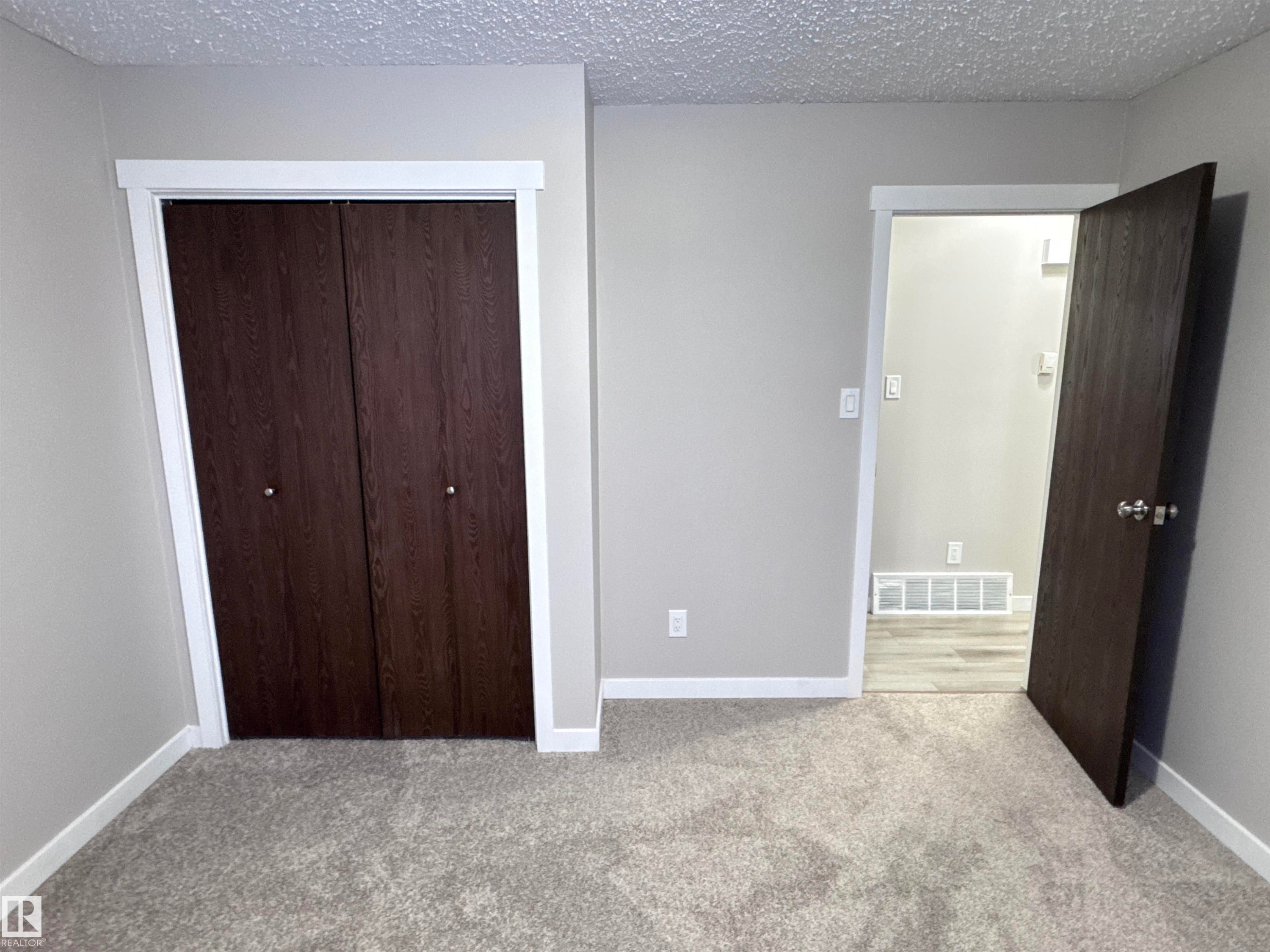 Unfurnished bedroom featuring a textured ceiling, a closet, and light carpet - 4919 49 Avenue, Vimy, AB - Indoor