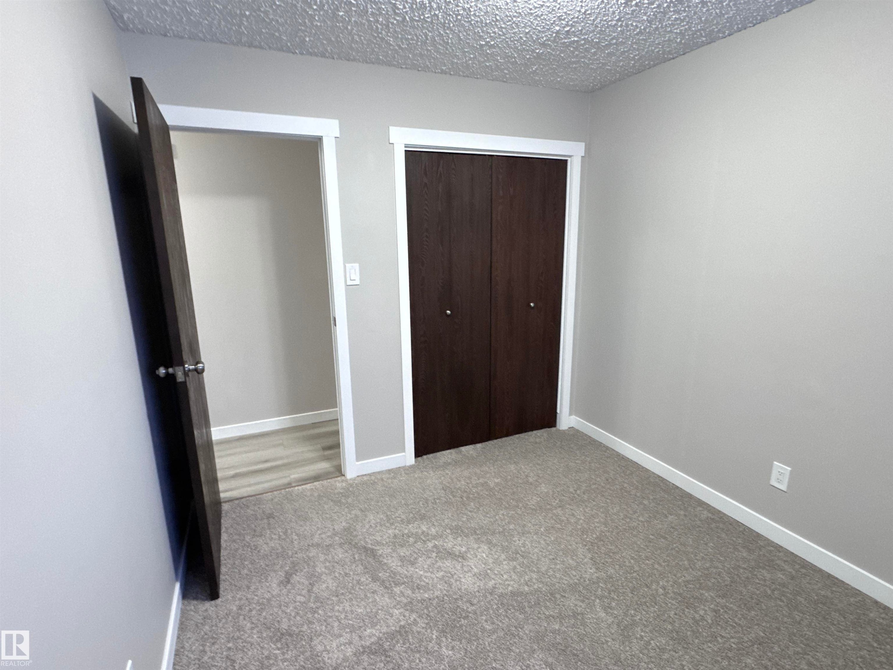 Unfurnished bedroom featuring light colored carpet, a textured ceiling, and a closet - 4919 49 Avenue, Vimy, AB - Indoor