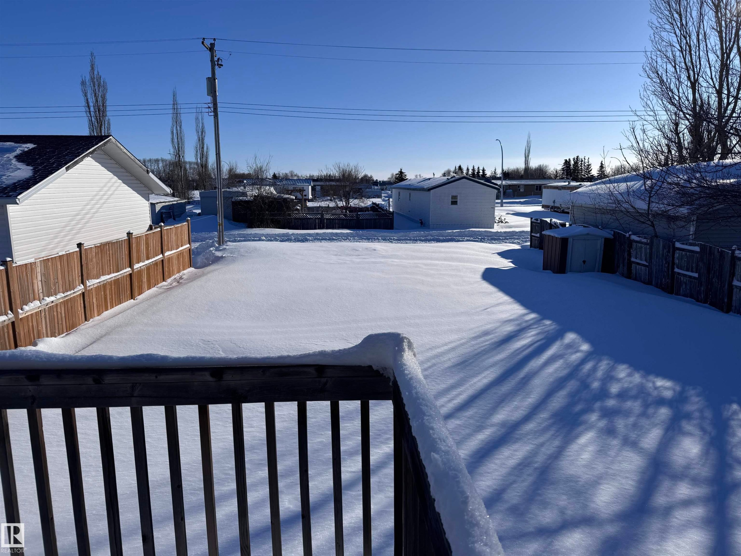 Yard layered in snow featuring a storage unit, a fenced backyard, and a residential view - 4919 49 Avenue, Vimy, AB - Outdoor