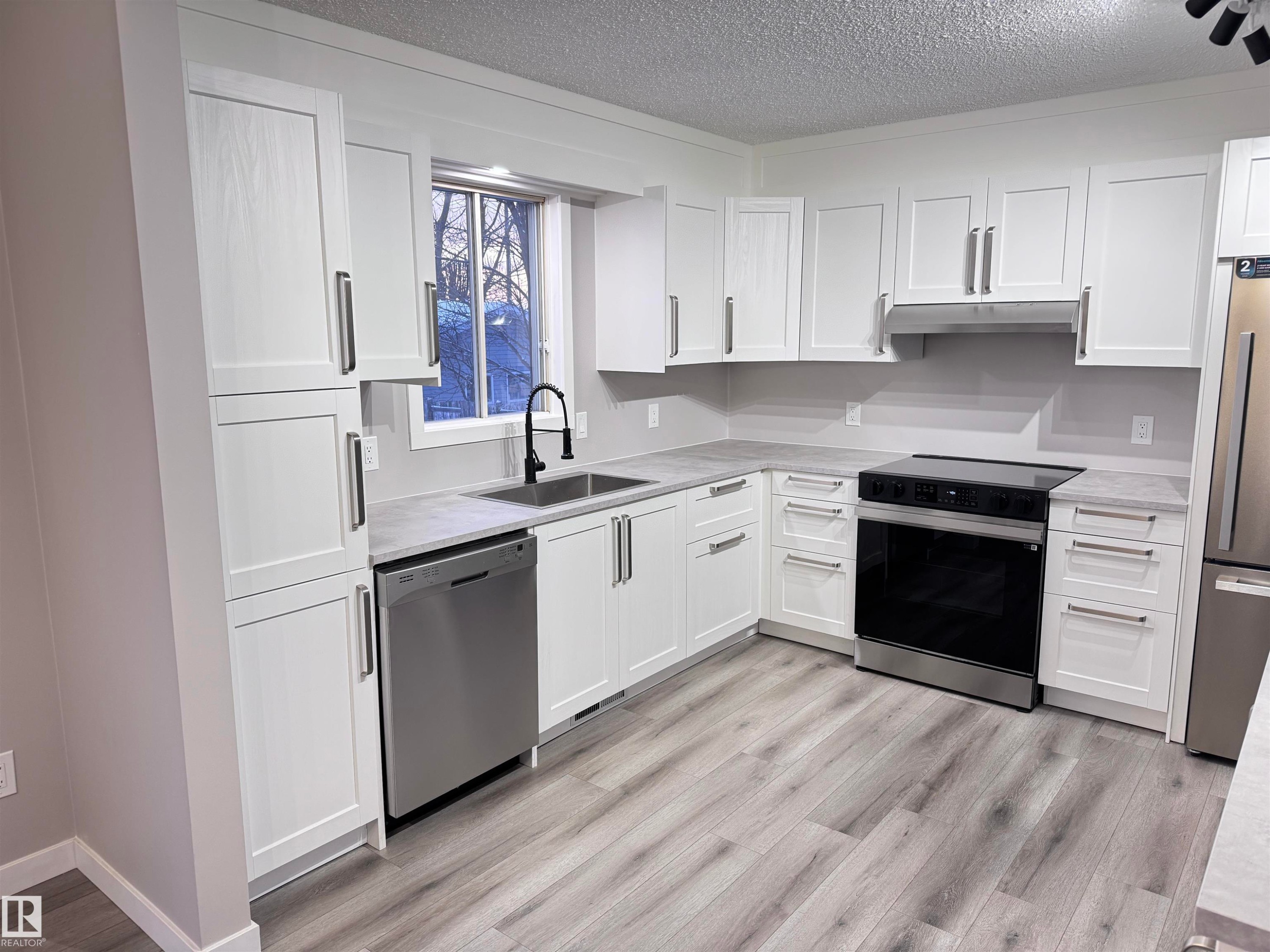 Kitchen with stainless steel appliances, a textured ceiling, white cabinetry, light wood-type flooring, and light stone countertops - 4919 49 Avenue, Vimy, AB - Indoor Photo Showing Kitchen