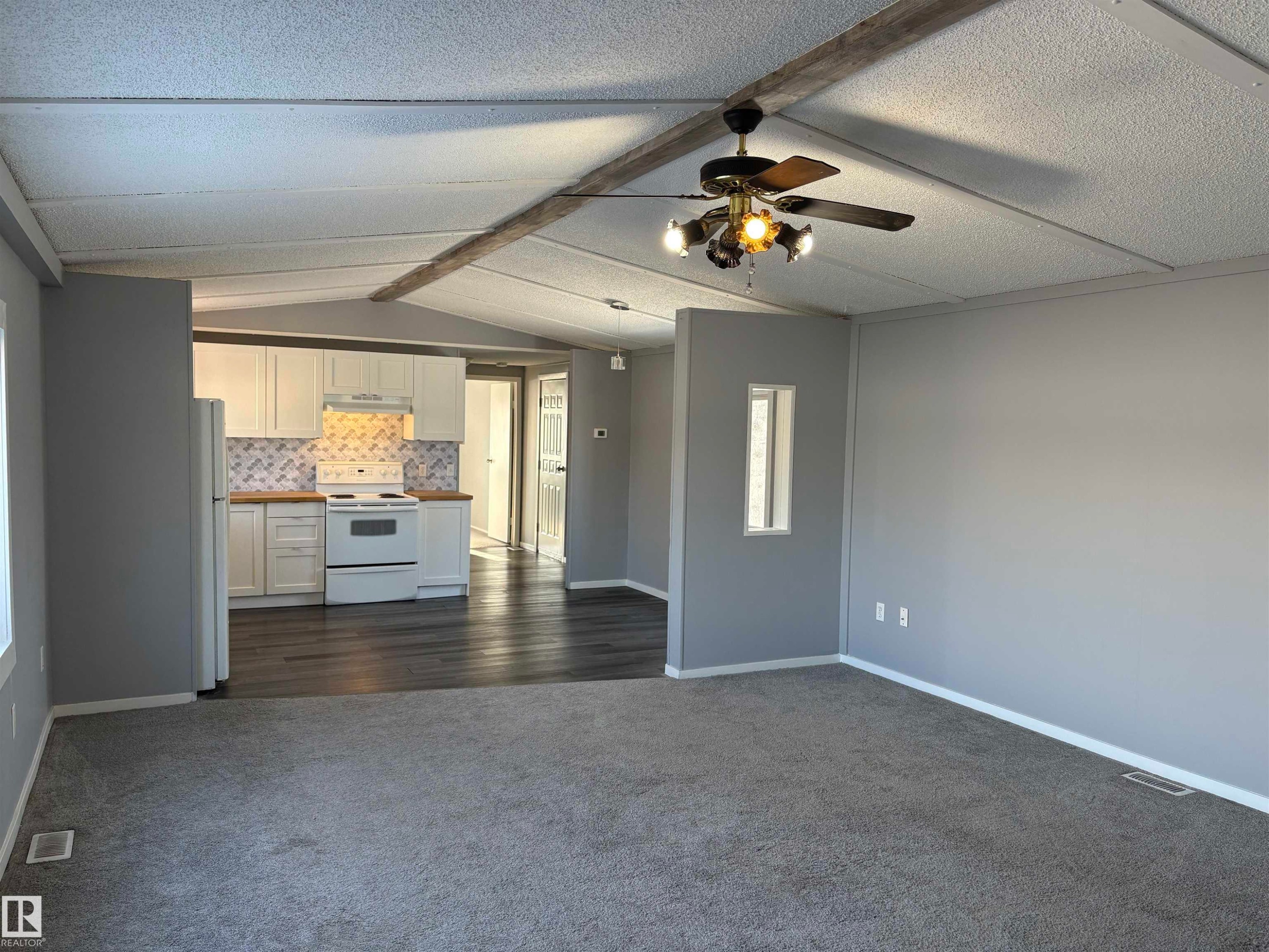 Unfurnished living room featuring dark colored carpet, ceiling fan, a textured ceiling, and beam ceiling - 8 Evergreen Park Drive, Edmonton, AB - Indoor