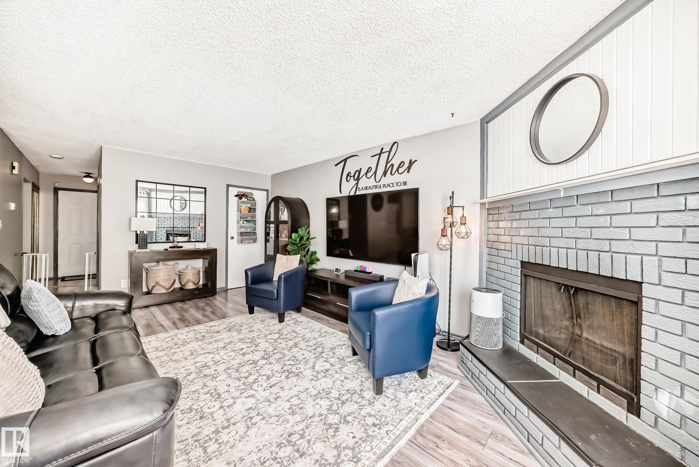 Living room with light wood-style flooring, a brick fireplace, and a textured ceiling - 214A Warwick Road, Edmonton, AB - Indoor Photo Showing Living Room With Fireplace