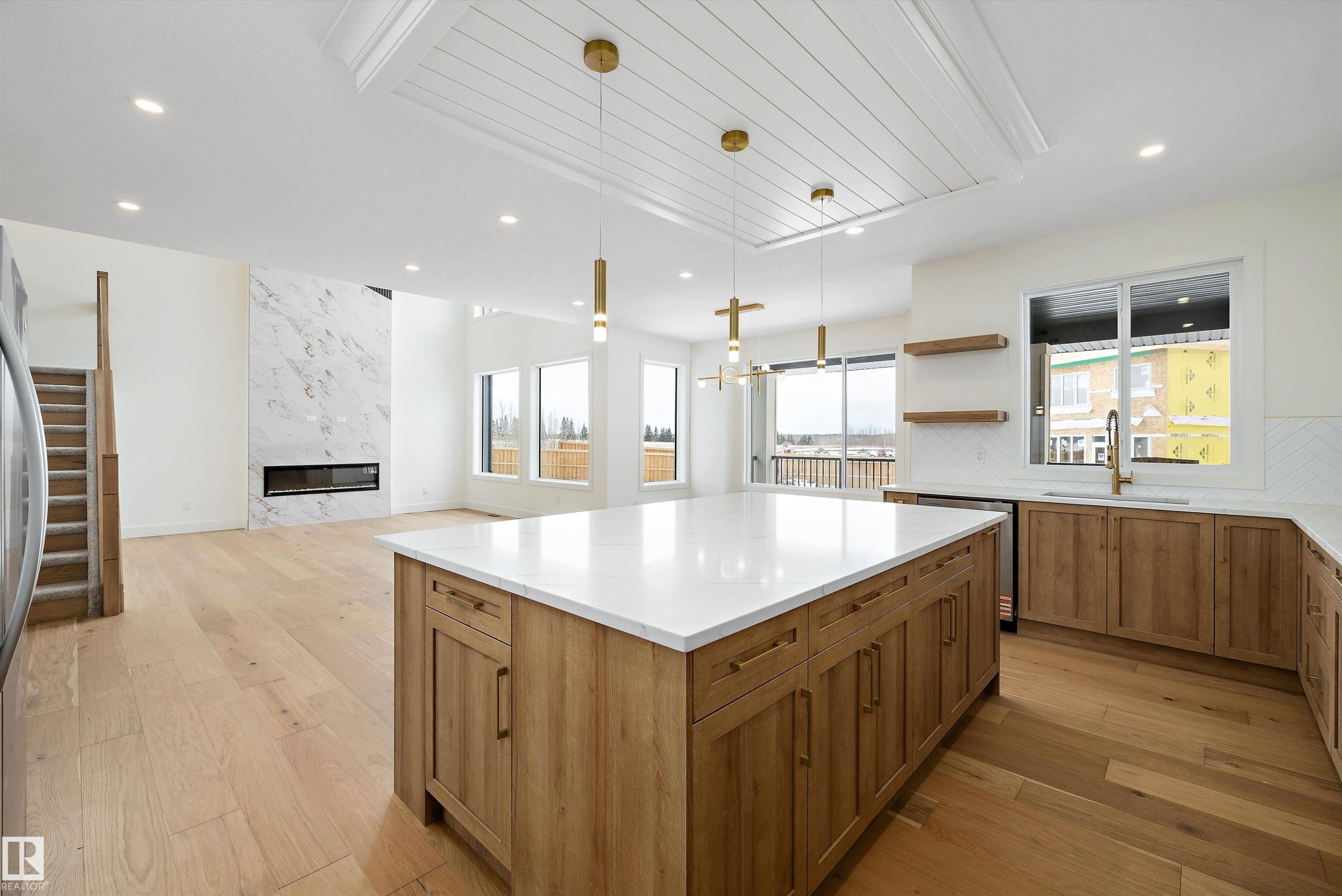 Kitchen with a kitchen island, a fireplace, light wood-style floors, and decorative light fixtures - 6871 Knox Loop Sw, Edmonton, AB - Indoor Photo Showing Kitchen With Upgraded Kitchen