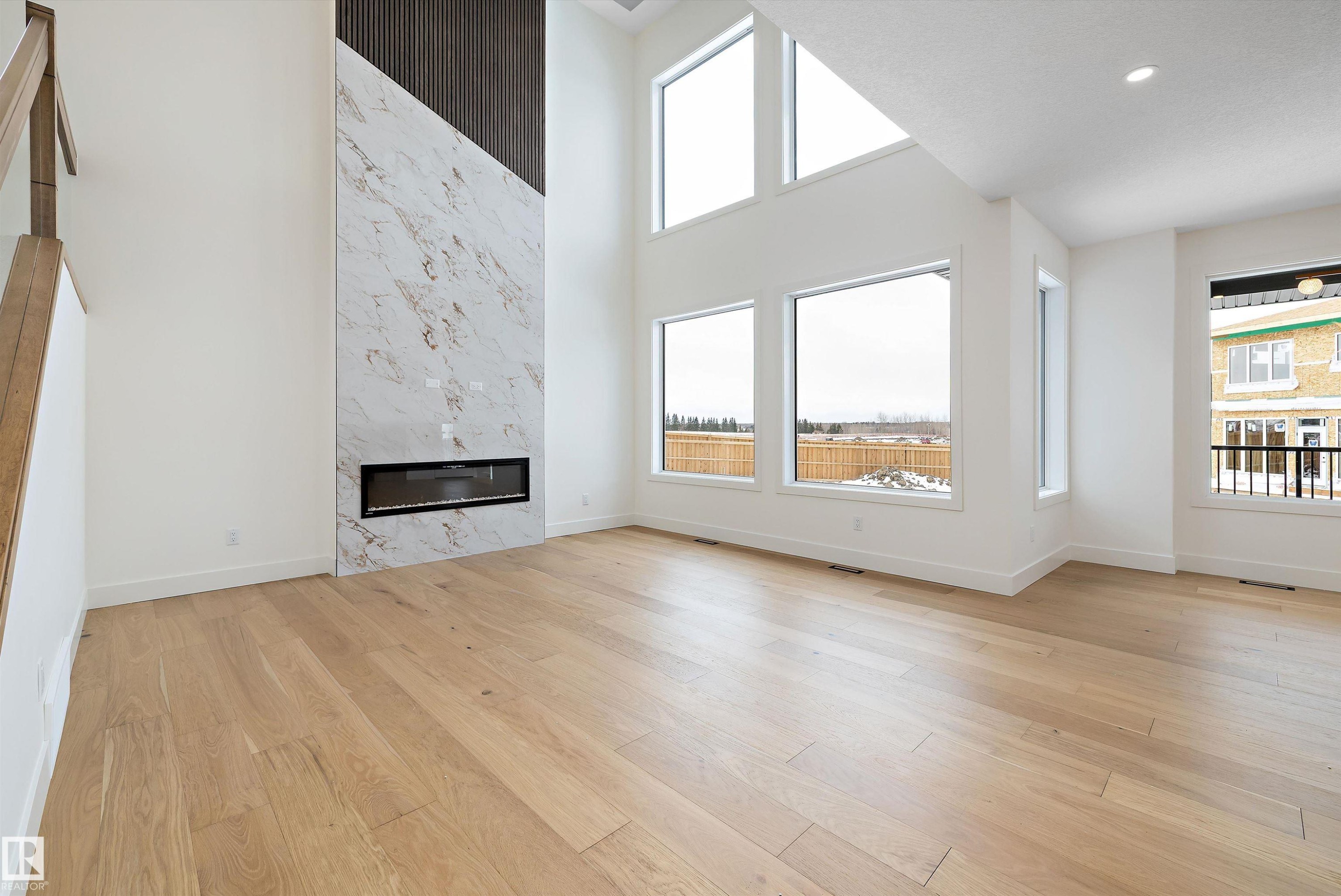 Unfurnished living room featuring a premium fireplace, a high ceiling, and light wood finished floors - 6871 Knox Loop Sw, Edmonton, AB - Indoor Photo Showing Living Room With Fireplace