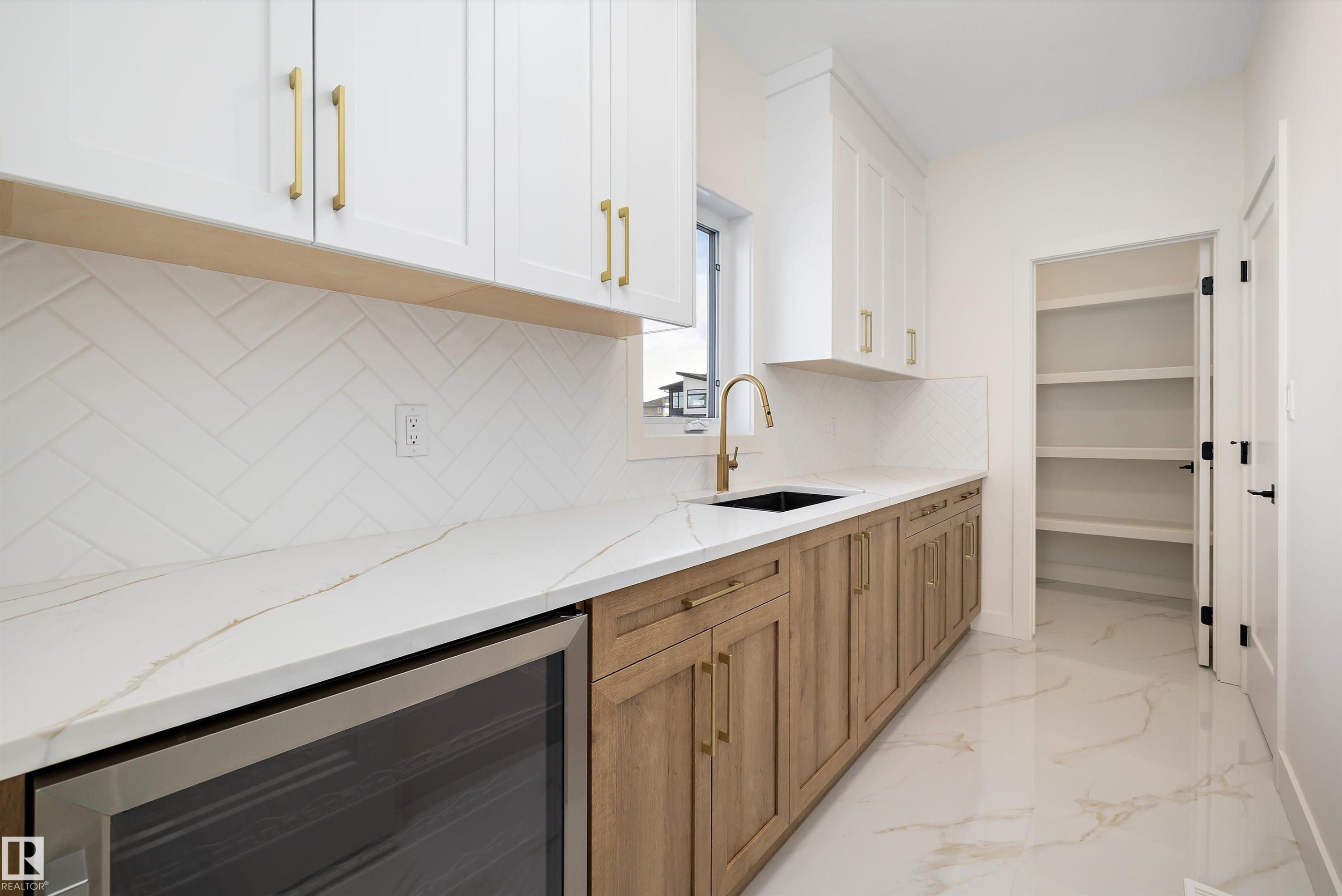 Kitchen with beverage cooler, two tone color scheme, light stone counters, decorative backsplash, and light marble finish floors - 6871 Knox Loop Sw, Edmonton, AB - Indoor Photo Showing Kitchen