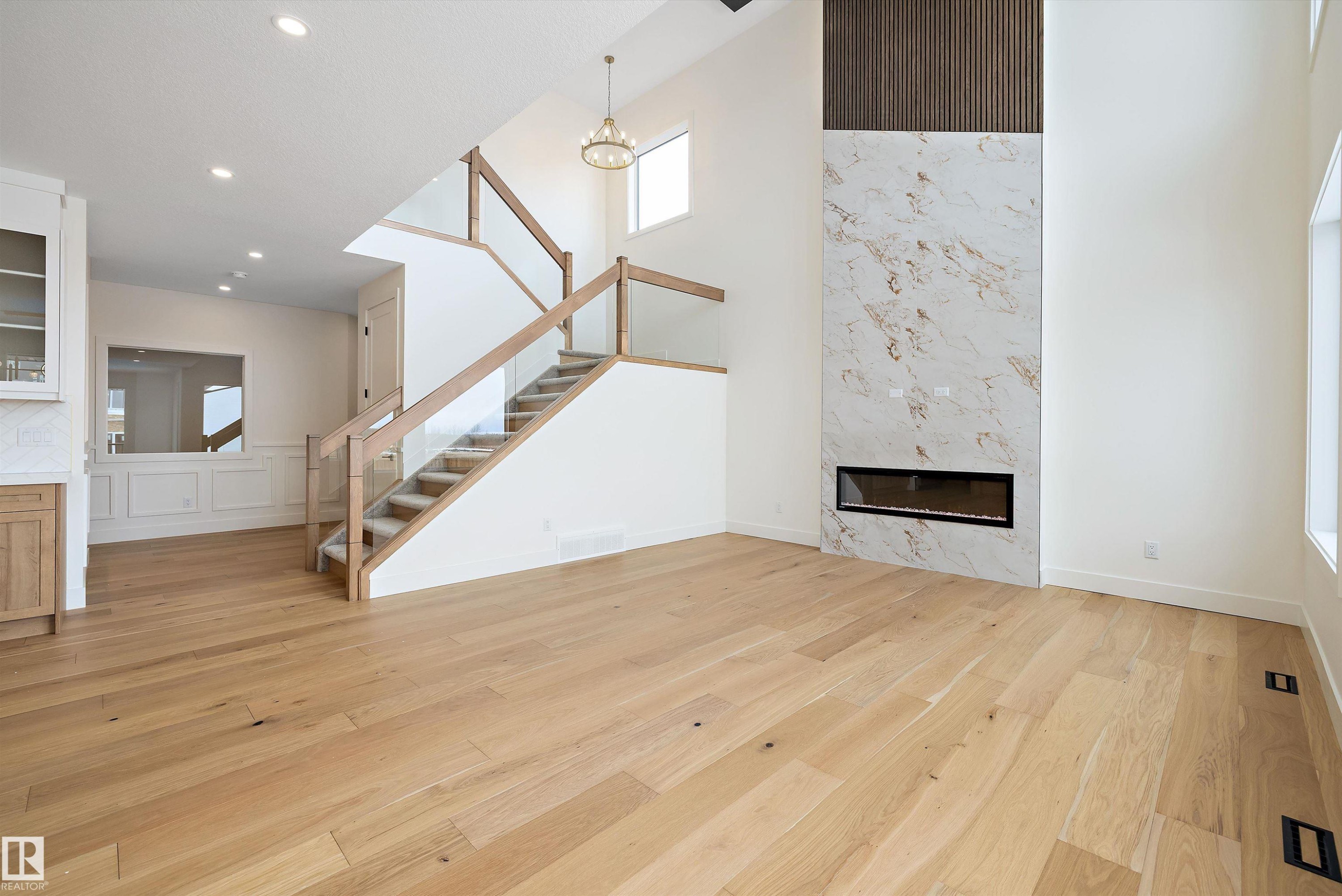 Unfurnished living room featuring a premium fireplace, light wood-style floors, a high ceiling, and recessed lighting - 6871 Knox Loop Sw, Edmonton, AB - Indoor With Fireplace