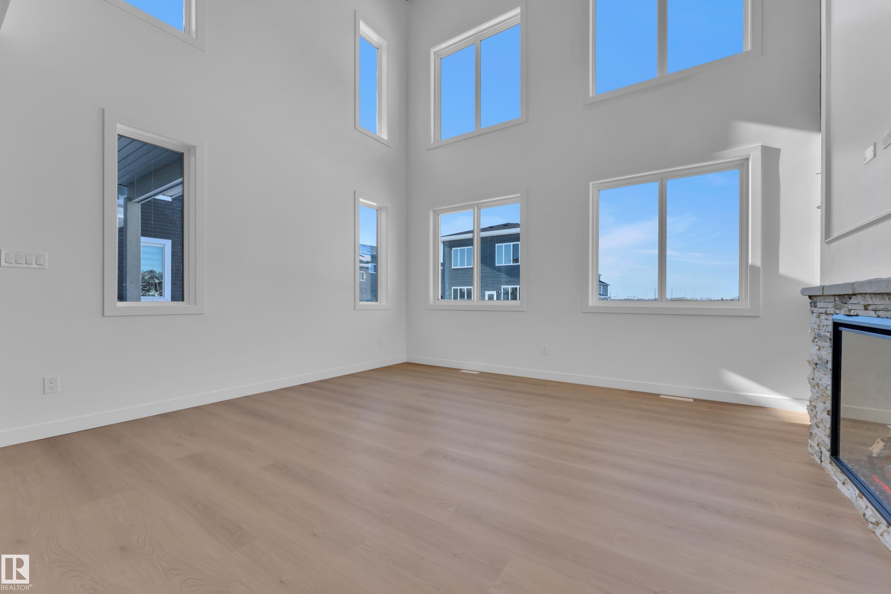 Unfurnished living room with a stone fireplace, light wood-type flooring, and a high ceiling - 95 Eldridge Point(E), St. Albert, AB - Indoor Photo Showing Other Room