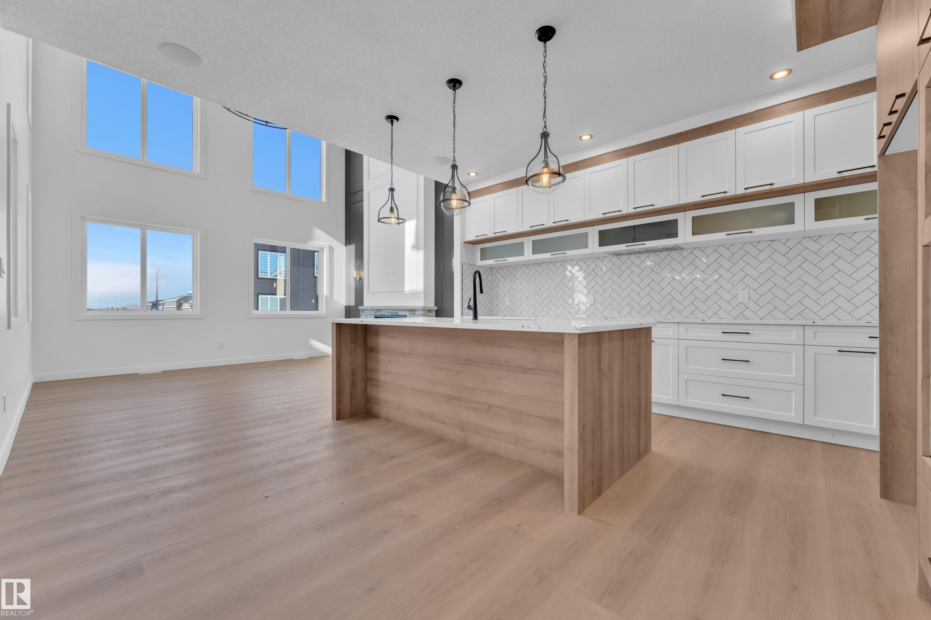 Two tone kitchen with dual tone cabinets, decorative light fixtures, an island with sink, light wood-style flooring, and decorative backsplash - 95 Eldridge Point(E), St. Albert, AB - Indoor Photo Showing Kitchen