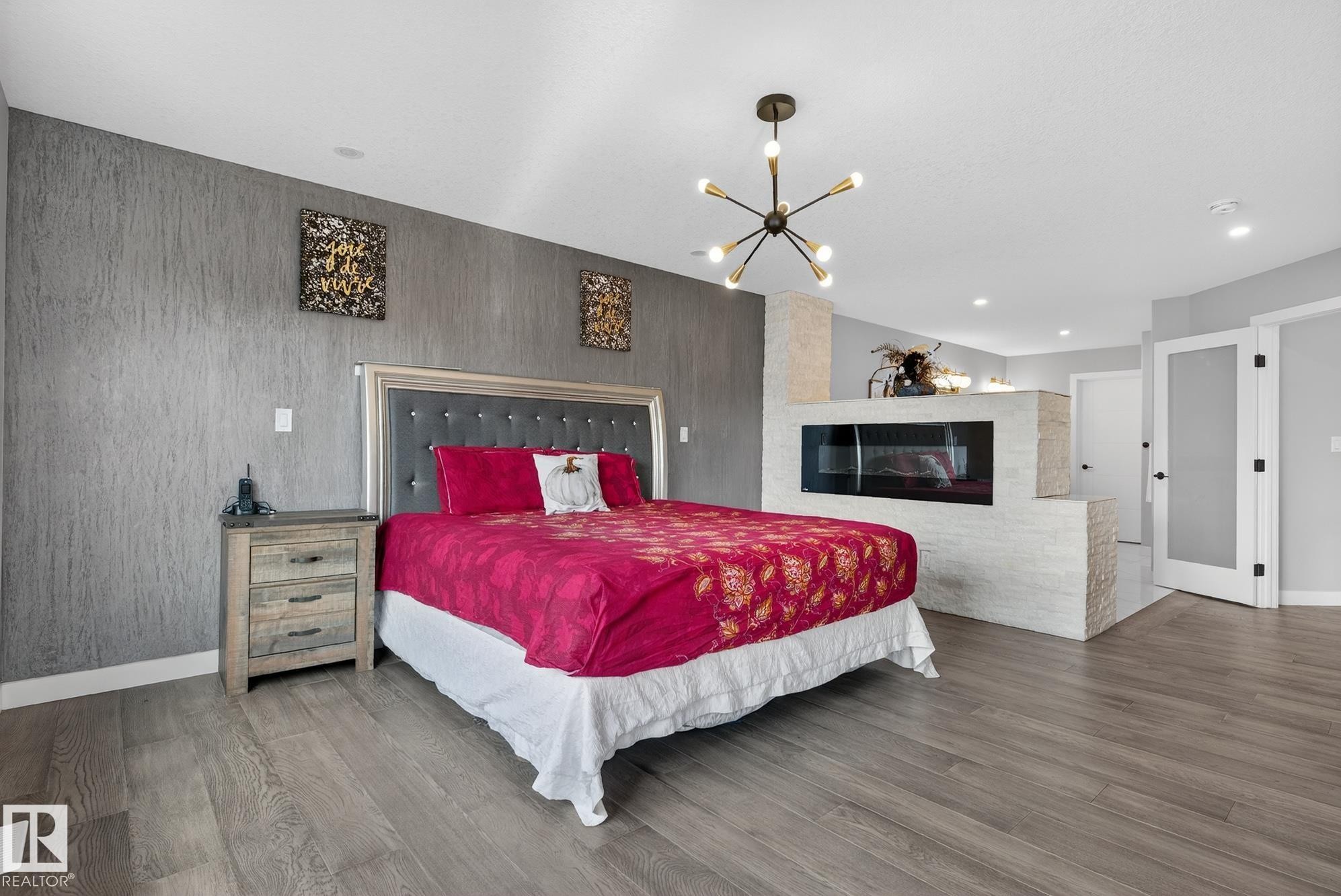 Bedroom with wood finished floors, a glass covered fireplace, and suspended lighting - 1027 150 Avenue, Edmonton, AB - Indoor Photo Showing Bedroom