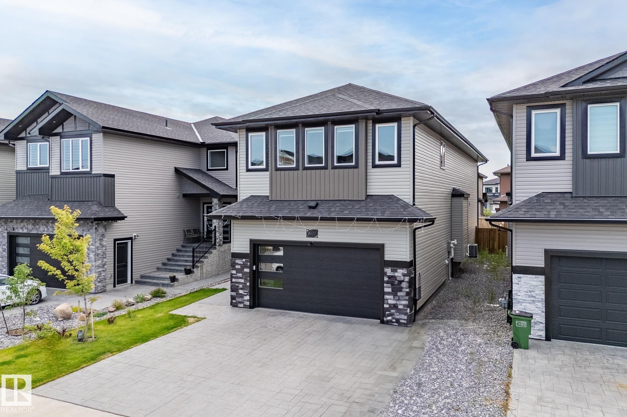 View of front of house with a shingled roof, decorative driveway, an attached garage, and stone siding - 1027 150 Avenue, Edmonton, AB - Outdoor With Facade