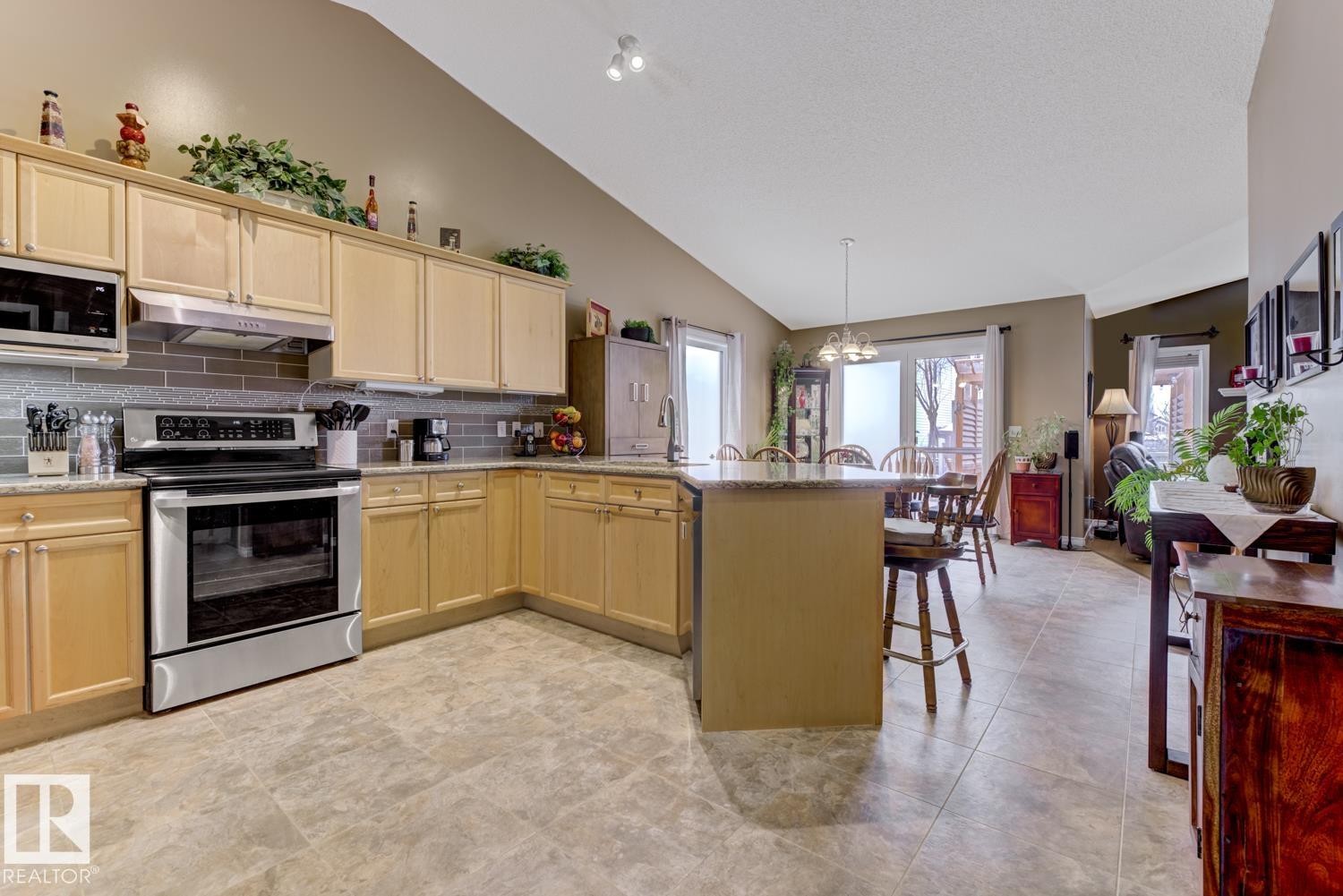 Kitchen with stainless steel appliances, a peninsula, lofted ceiling, light wood finish cabinets, and a kitchen bar - 20148 46 Avenue, Edmonton, AB - Indoor Photo Showing Kitchen