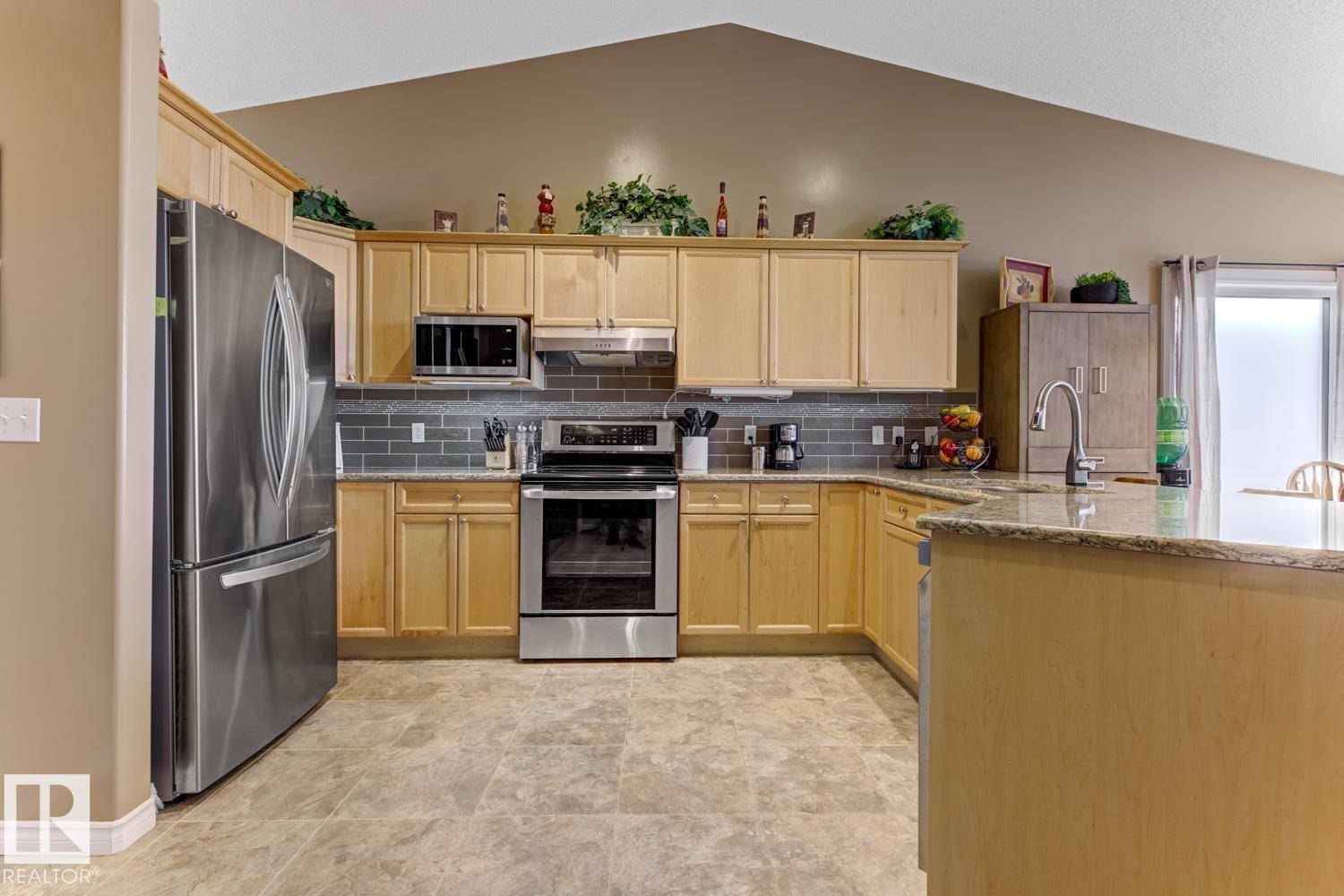 Kitchen with stainless steel appliances, light stone counters, light wood finish cabinetry, decorative backsplash, and lofted ceiling - 20148 46 Avenue, Edmonton, AB - Indoor Photo Showing Kitchen With Stainless Steel Kitchen With Double Sink
