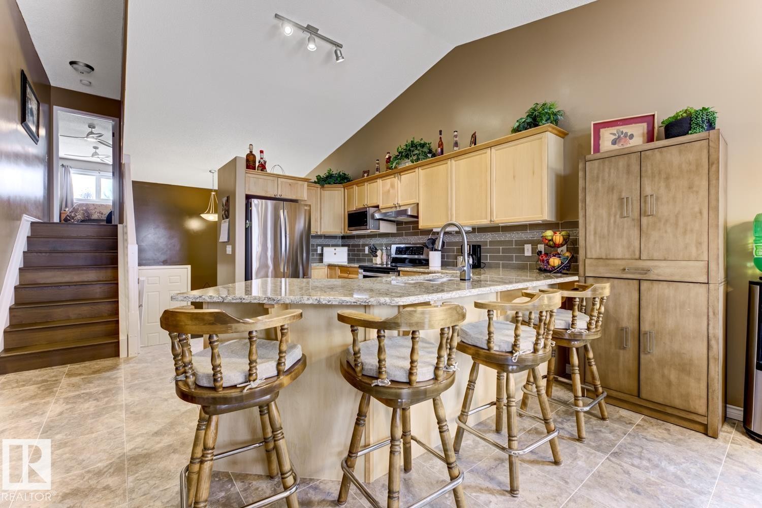 Kitchen with light wood finish cabinetry, light stone countertops, stainless steel appliances, a peninsula, and lofted ceiling - 20148 46 Avenue, Edmonton, AB - Indoor