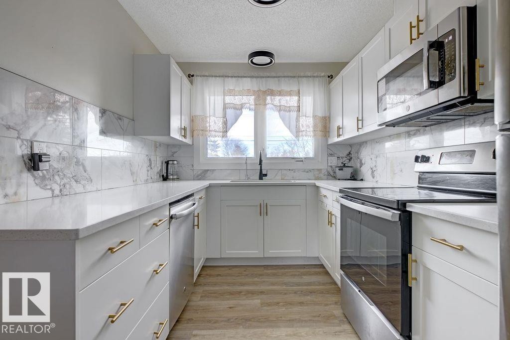 Kitchen featuring stainless steel appliances, a textured ceiling, white cabinetry, light wood-type flooring, and light stone counters - 13211 71 Street, Edmonton, AB - Indoor Photo Showing Kitchen