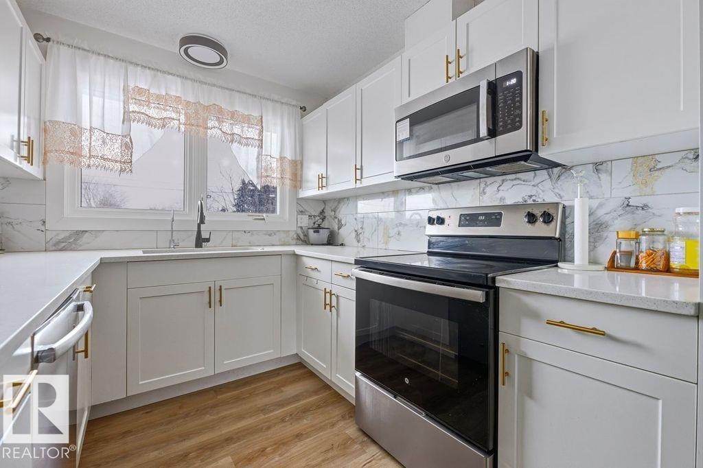 Kitchen featuring stainless steel appliances, white cabinets, light wood-type flooring, a textured ceiling, and light stone countertops - 13211 71 Street, Edmonton, AB - Indoor Photo Showing Kitchen