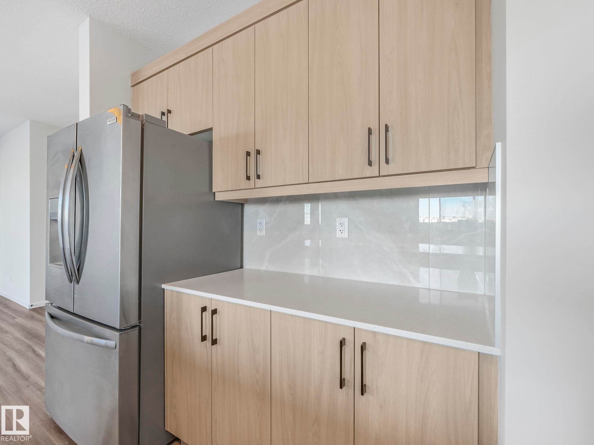 Kitchen featuring light wood finish cabinets, stainless steel fridge, modern cabinets, light wood-style floors, and decorative backsplash - 20506 16A Avenue, Edmonton, AB - Indoor Photo Showing Kitchen
