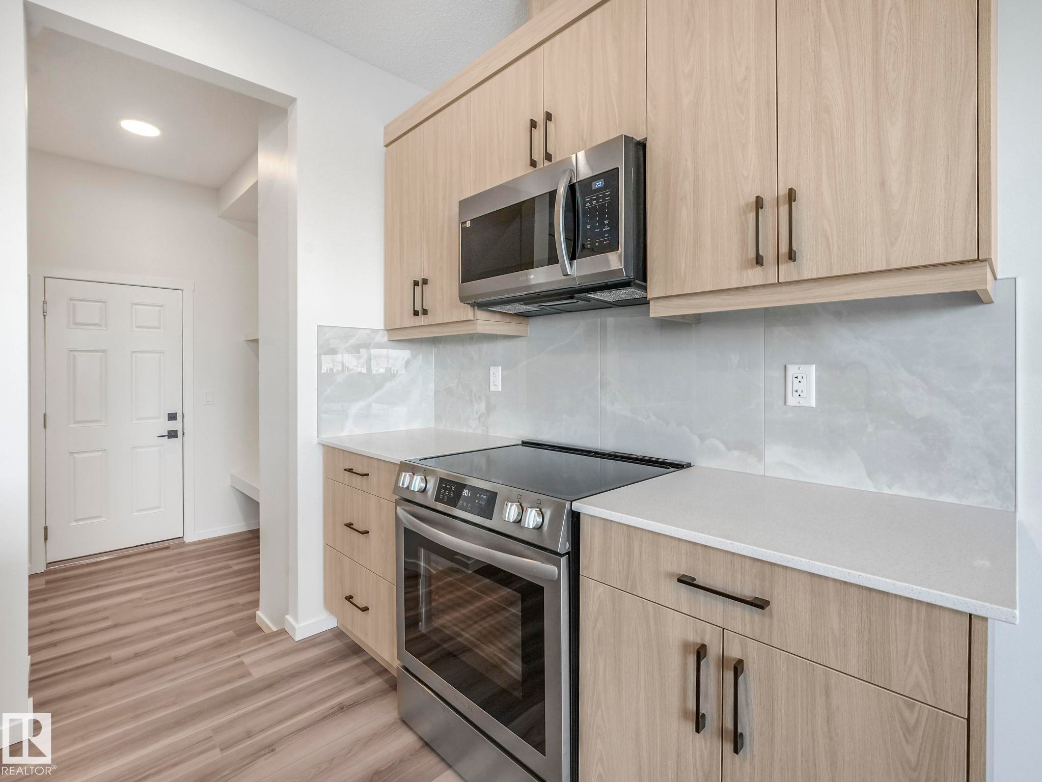 Kitchen with stainless steel appliances, light wood finish cabinetry, backsplash, and light stone countertops - 20506 16A Avenue, Edmonton, AB - Indoor Photo Showing Kitchen