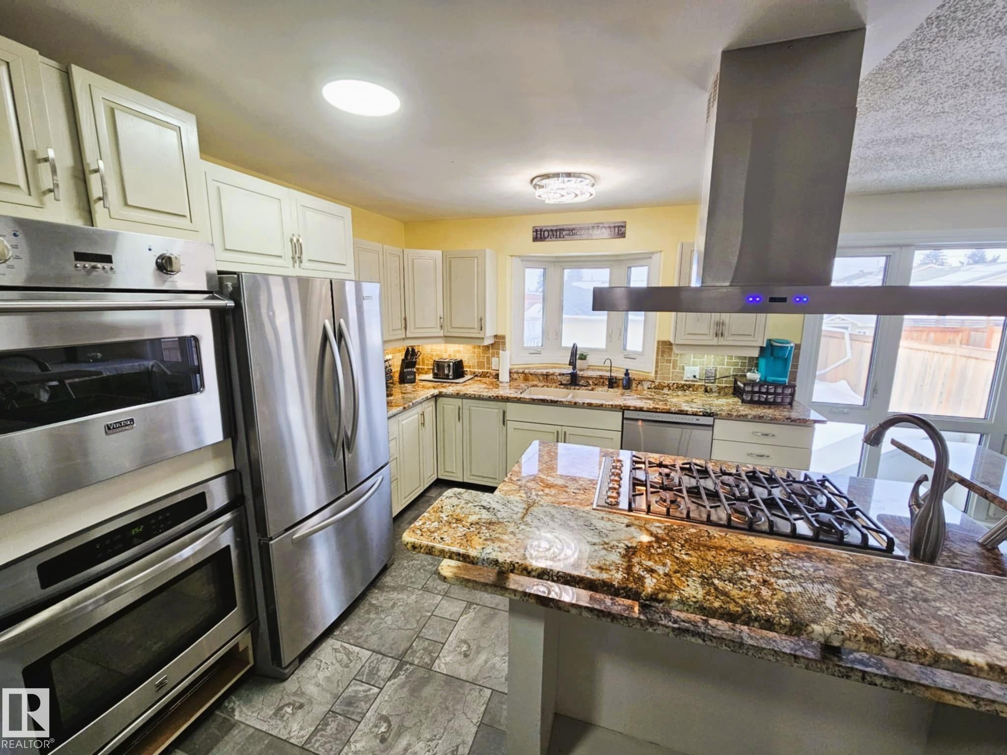 Kitchen featuring stainless steel appliances, dark stone counters, island exhaust hood, backsplash, and white cabinetry - 8512 131 Avenue, Edmonton, AB - Indoor Photo Showing Kitchen With Upgraded Kitchen