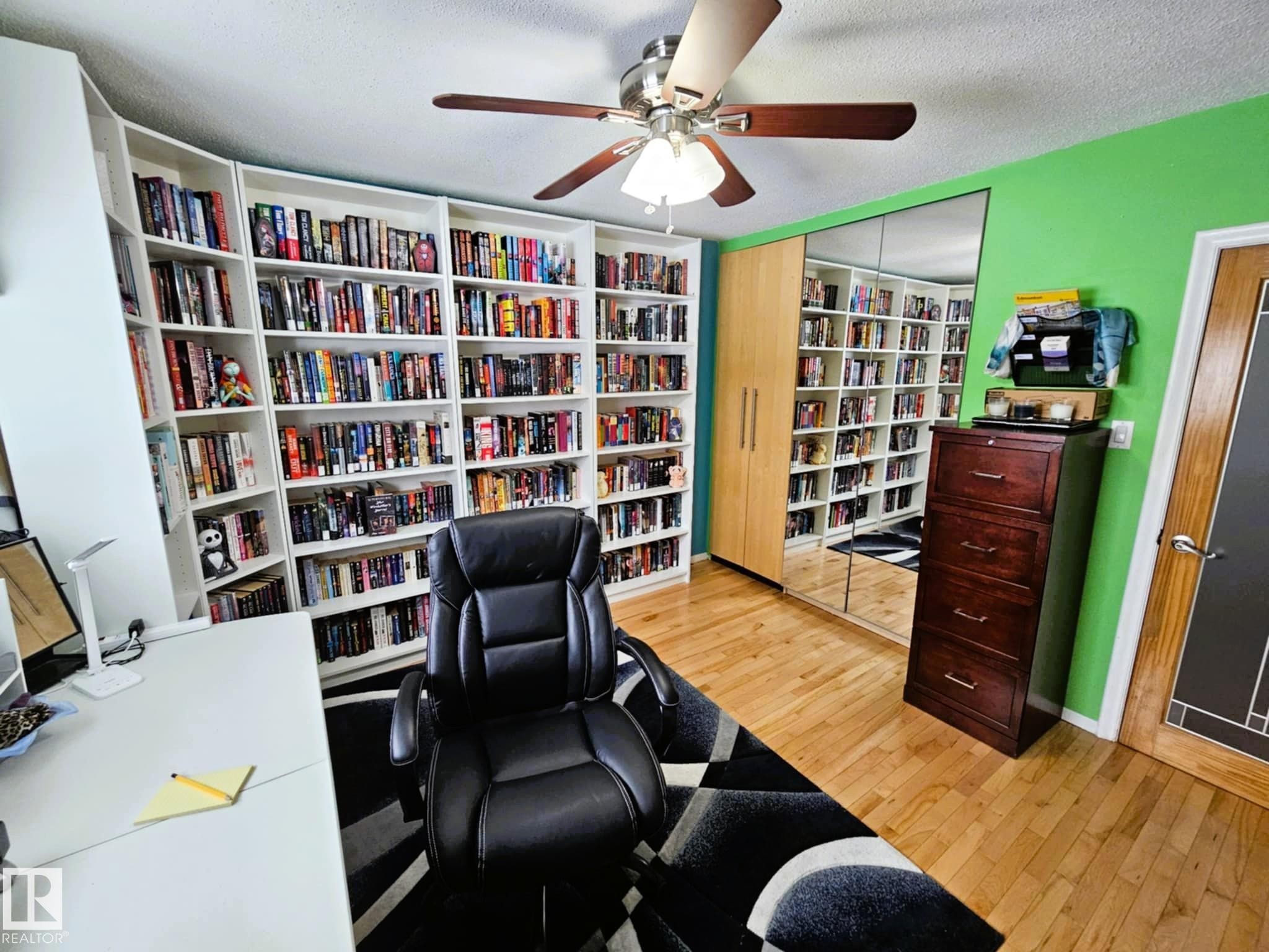 Office area with light wood-style flooring, ceiling fan, wall of books, and a textured ceiling - 8512 131 Avenue, Edmonton, AB - Indoor Photo Showing Office