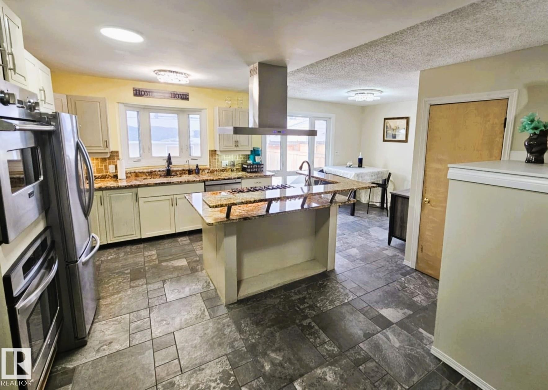 Kitchen with island exhaust hood, light stone countertops, decorative backsplash, an island with sink, and stainless steel appliances - 8512 131 Avenue, Edmonton, AB - Indoor Photo Showing Kitchen With Upgraded Kitchen