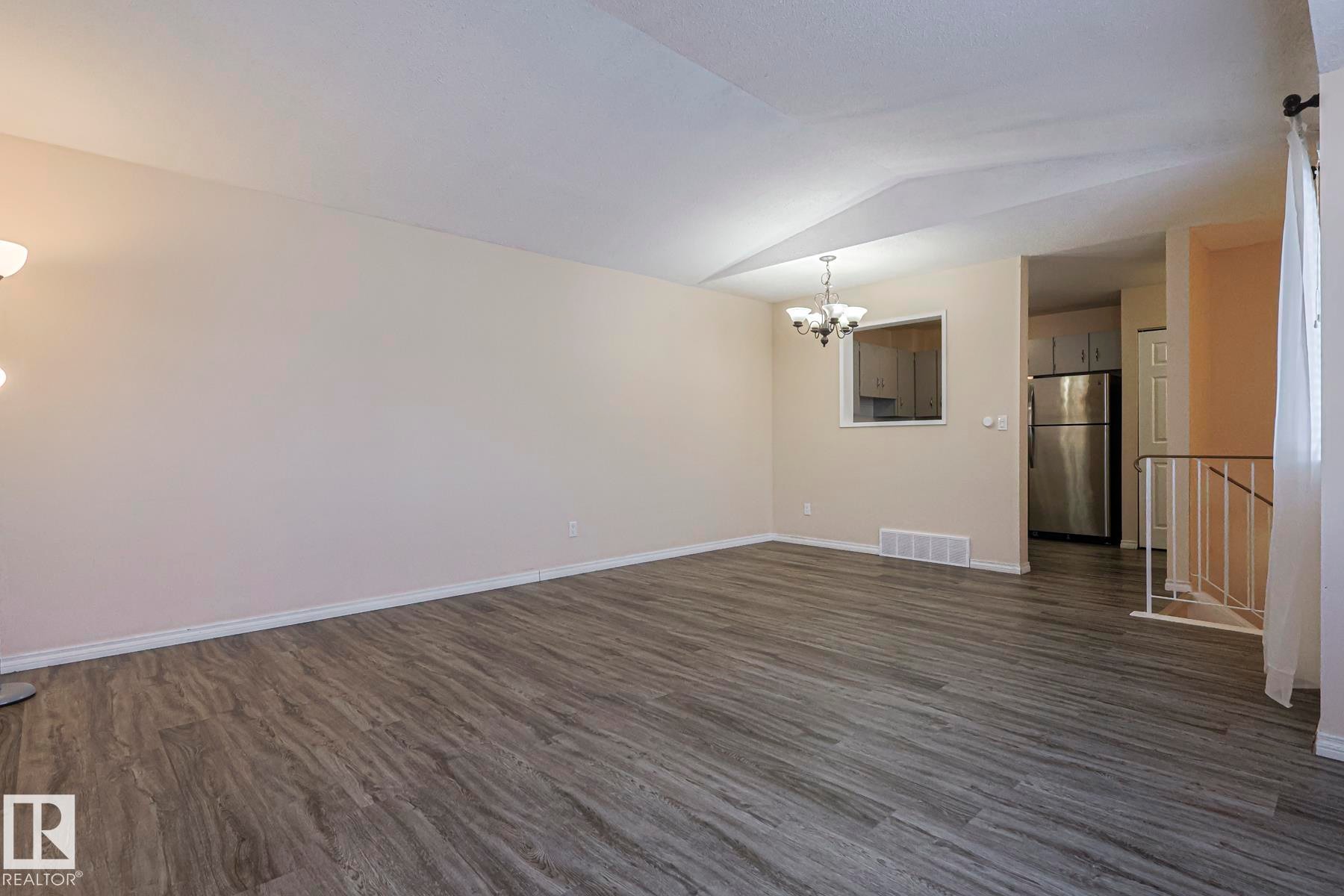 Unfurnished living room with hanging lights, dark wood-type flooring, and lofted ceiling - 1526 69 Street Nw, Edmonton, AB - Indoor Photo Showing Other Room