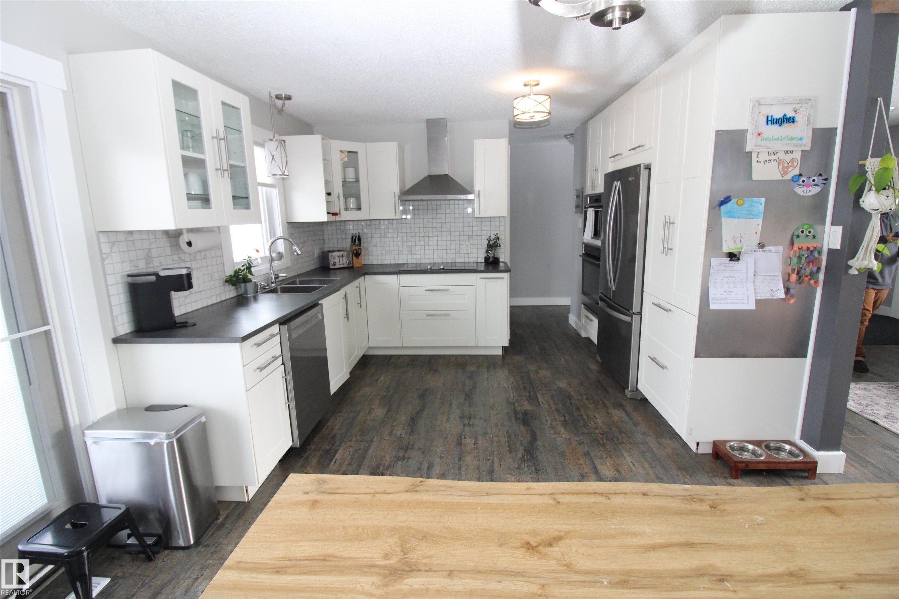 Kitchen with dark countertops, white cabinetry, glass fronted cabinets, dark wood finished floors, and stainless steel appliances - 10319 106 Ave, Westlock, AB - Indoor Photo Showing Kitchen With Double Sink