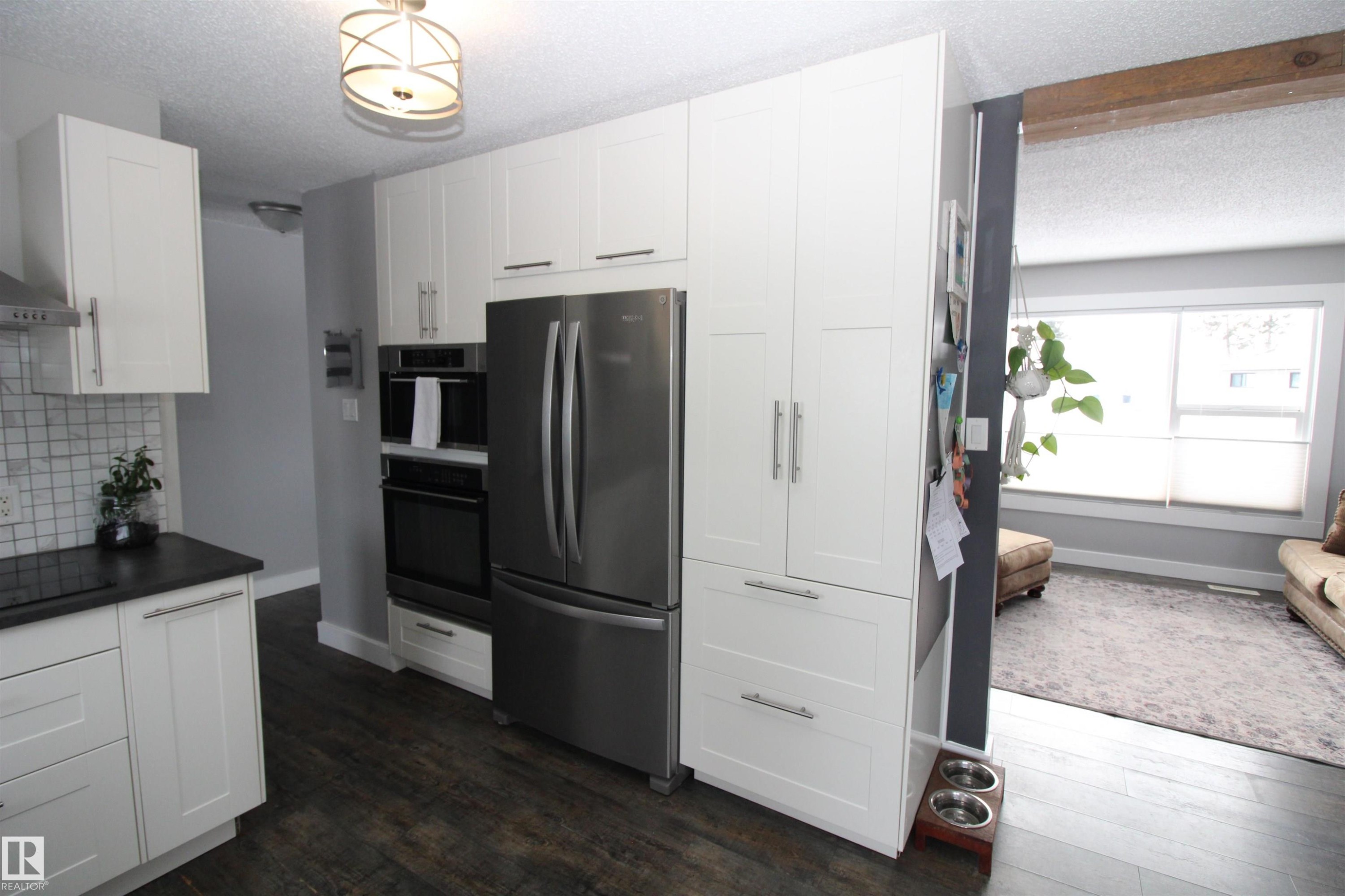 Kitchen with a textured ceiling, freestanding refrigerator, white cabinetry, dark wood-type flooring, and decorative backsplash - 10319 106 Ave, Westlock, AB - Indoor Photo Showing Kitchen