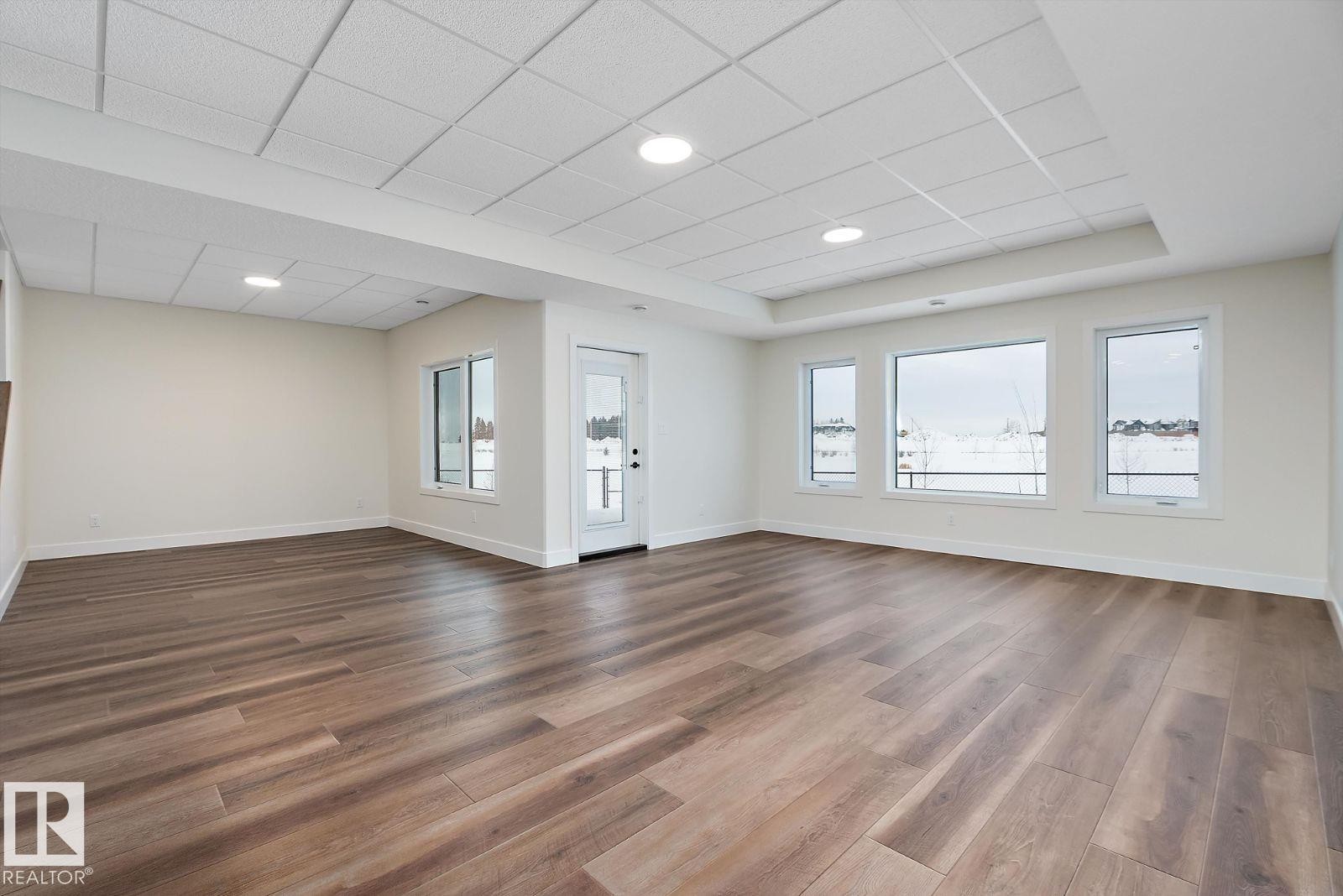 Unfurnished living room with plenty of natural light, dark wood-style flooring, a tray ceiling, and a paneled ceiling - 128 Lilac Close, Leduc, AB - Indoor Photo Showing Other Room