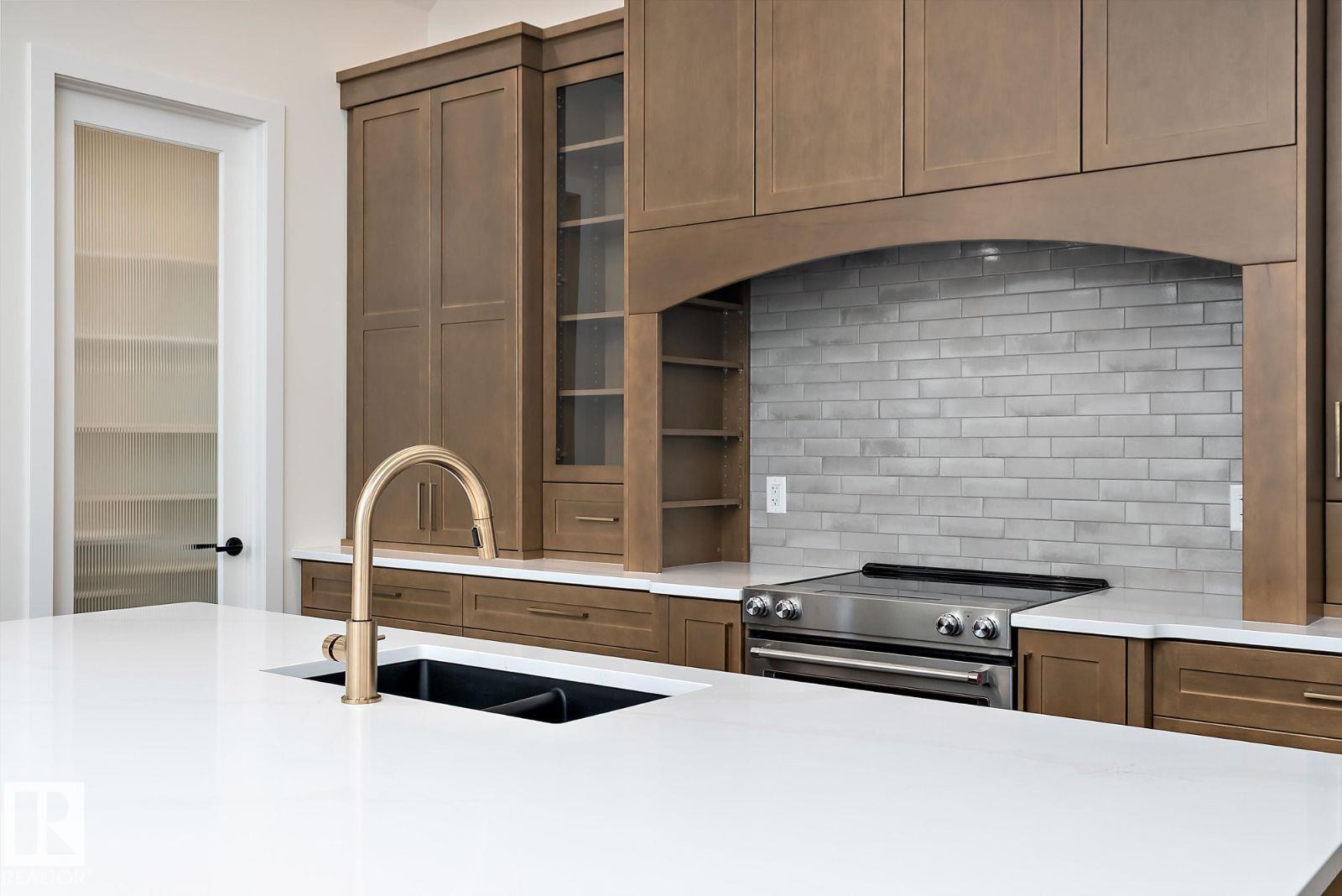 Kitchen featuring stainless steel range with electric stovetop, glass insert cabinets, light stone countertops, and decorative backsplash - 128 Lilac Close, Leduc, AB - Indoor Photo Showing Kitchen With Double Sink