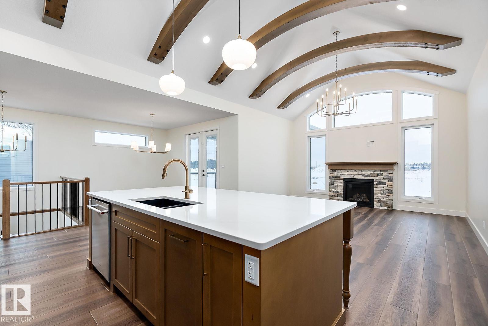 Kitchen with suspended lighting, dark wood finished floors, a center island with sink, beam ceiling, and a barrel ceiling - 128 Lilac Close, Leduc, AB - Indoor Photo Showing Kitchen With Fireplace