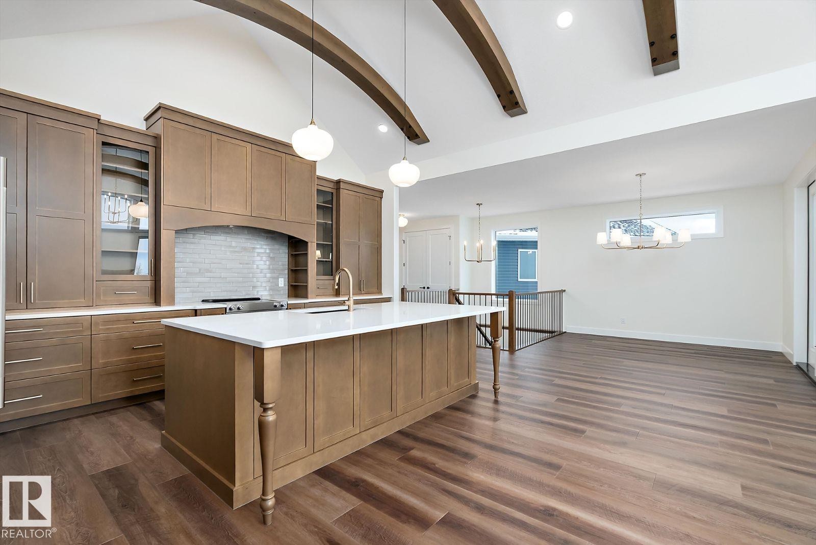 Kitchen featuring glass fronted cabinets, lofted ceiling, wood finish cabinets, dark wood-type flooring, and an island with sink - 128 Lilac Close, Leduc, AB - Indoor Photo Showing Kitchen With Upgraded Kitchen