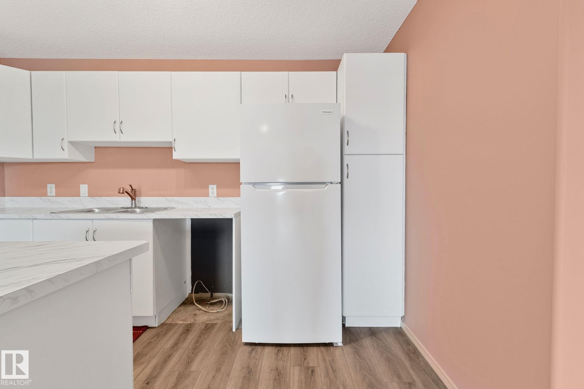 Kitchen with freestanding refrigerator, white cabinets, light countertops, light wood finished floors, and a textured ceiling - 406 16035 132 Street Nw, Edmonton, AB - Indoor Photo Showing Kitchen